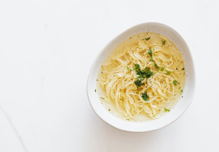 A bowl of chicken soup with large noodles in it