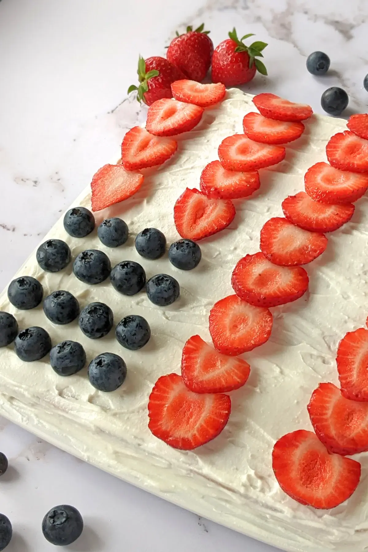 American flag sheet pan pancake decorated with ricotta frosting, strawberries, and blueberries to resemble the American flag.