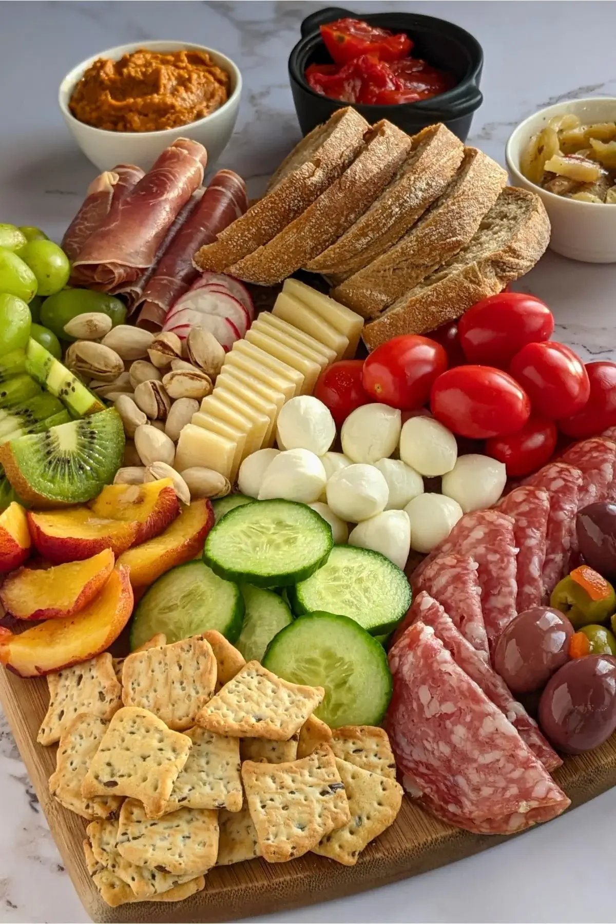 Vibrant antipasto board with salami, prosciutto, marinated veggies, cheeses, olives, fruit, and fresh bread.
