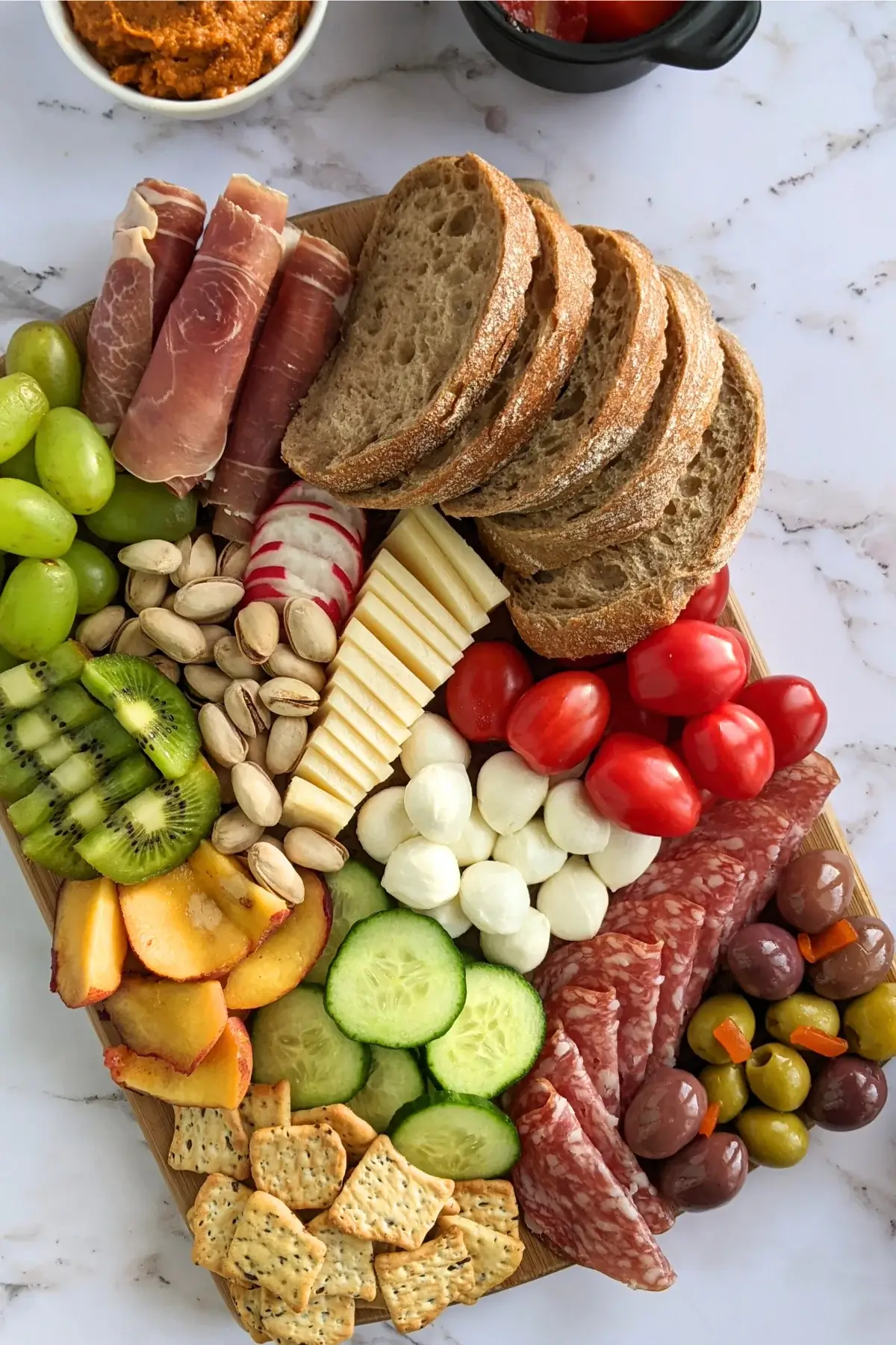 A vibrant antipasto board featuring salami, prosciutto, marinated tomatoes, olives, cheese, and fresh fruit.