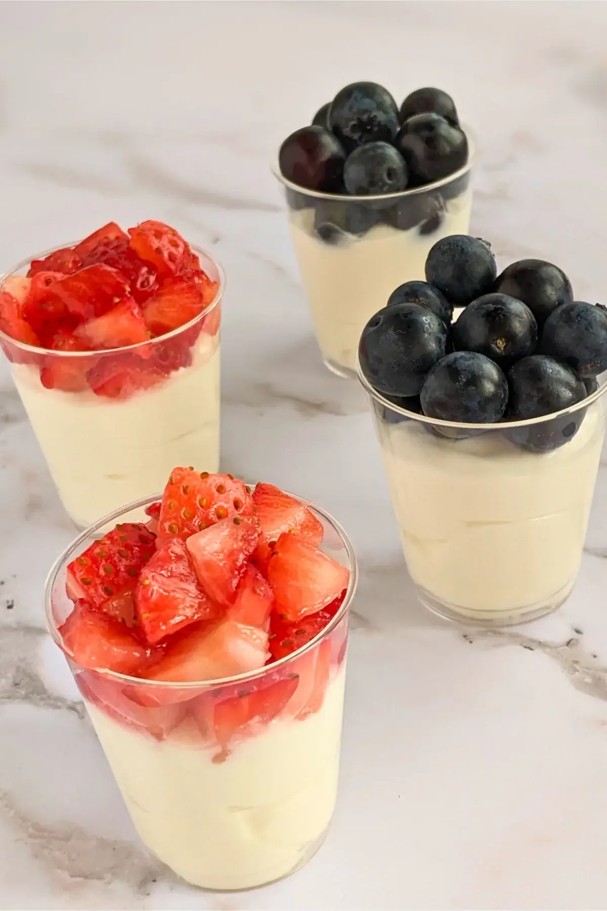 Patriotic mascarpone dessert shooters topped with either blueberries or strawberries in small glass cups.