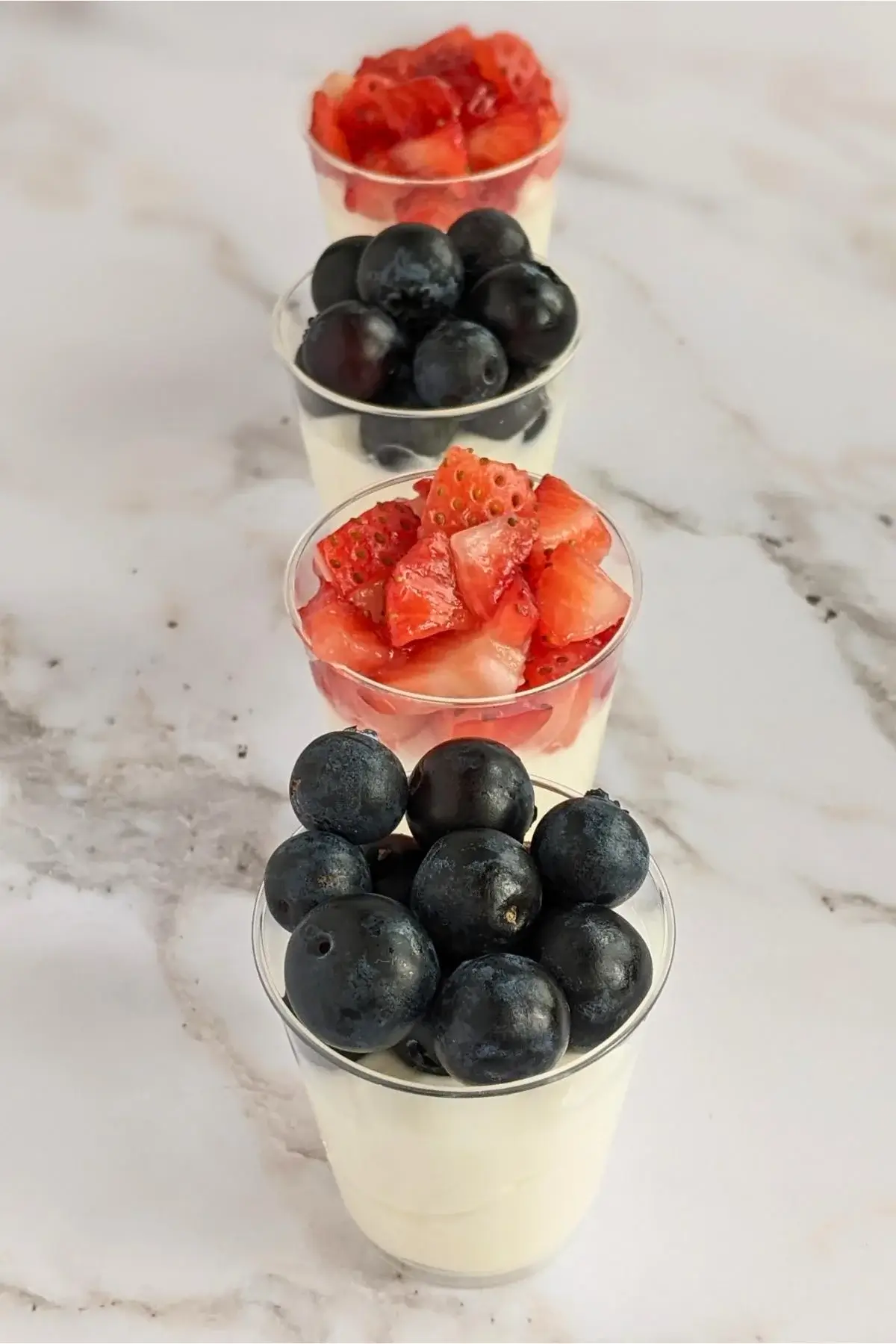 Individual dessert shooters with mascarpone and Greek yogurt mix, topped with either strawberries or blueberries.