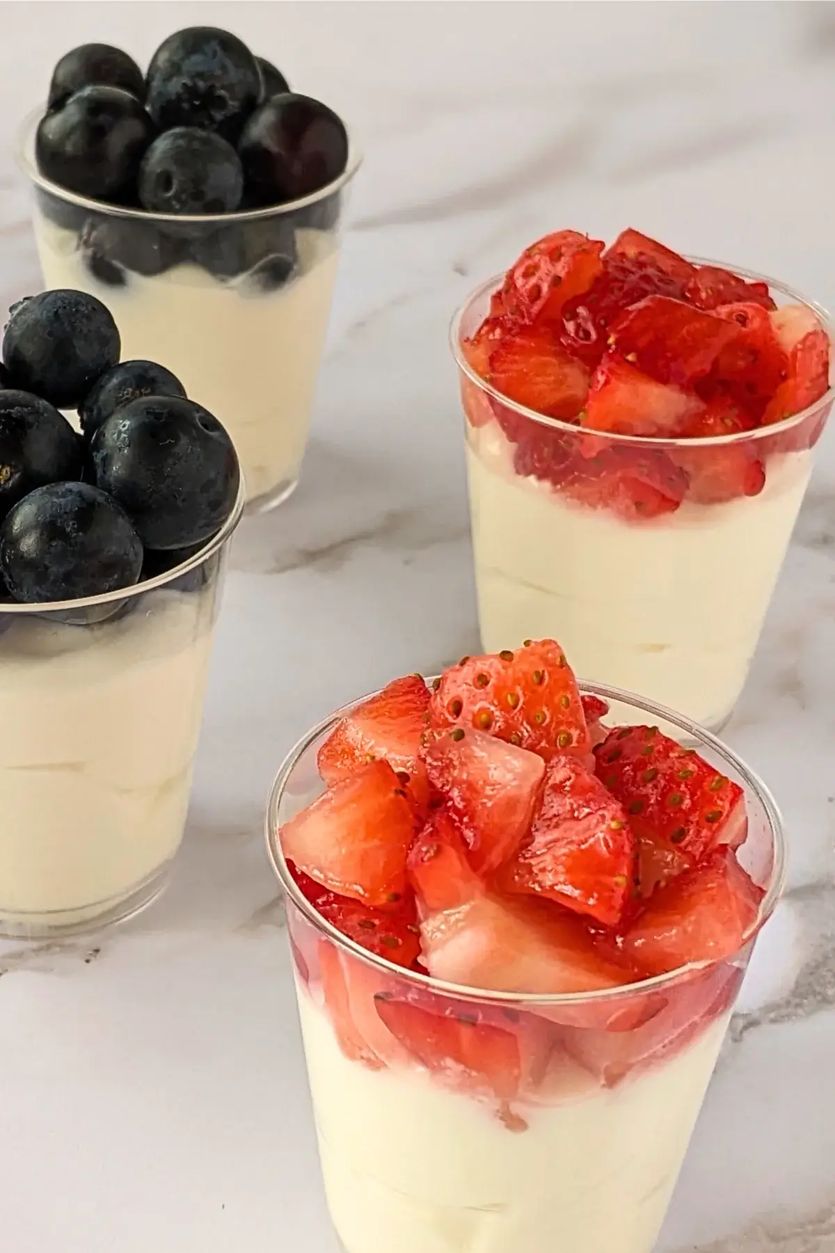 Berry dessert shooters with layers of mascarpone, Greek yogurt, and topped with either strawberries or blueberries.