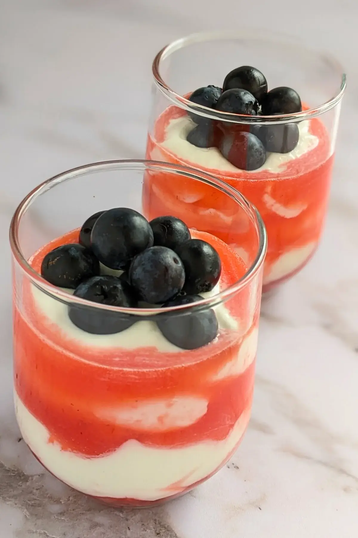 Patriotic whipped cream and Greek yogurt cups layered with strawberries, cream, strawberry juice, and blueberries.