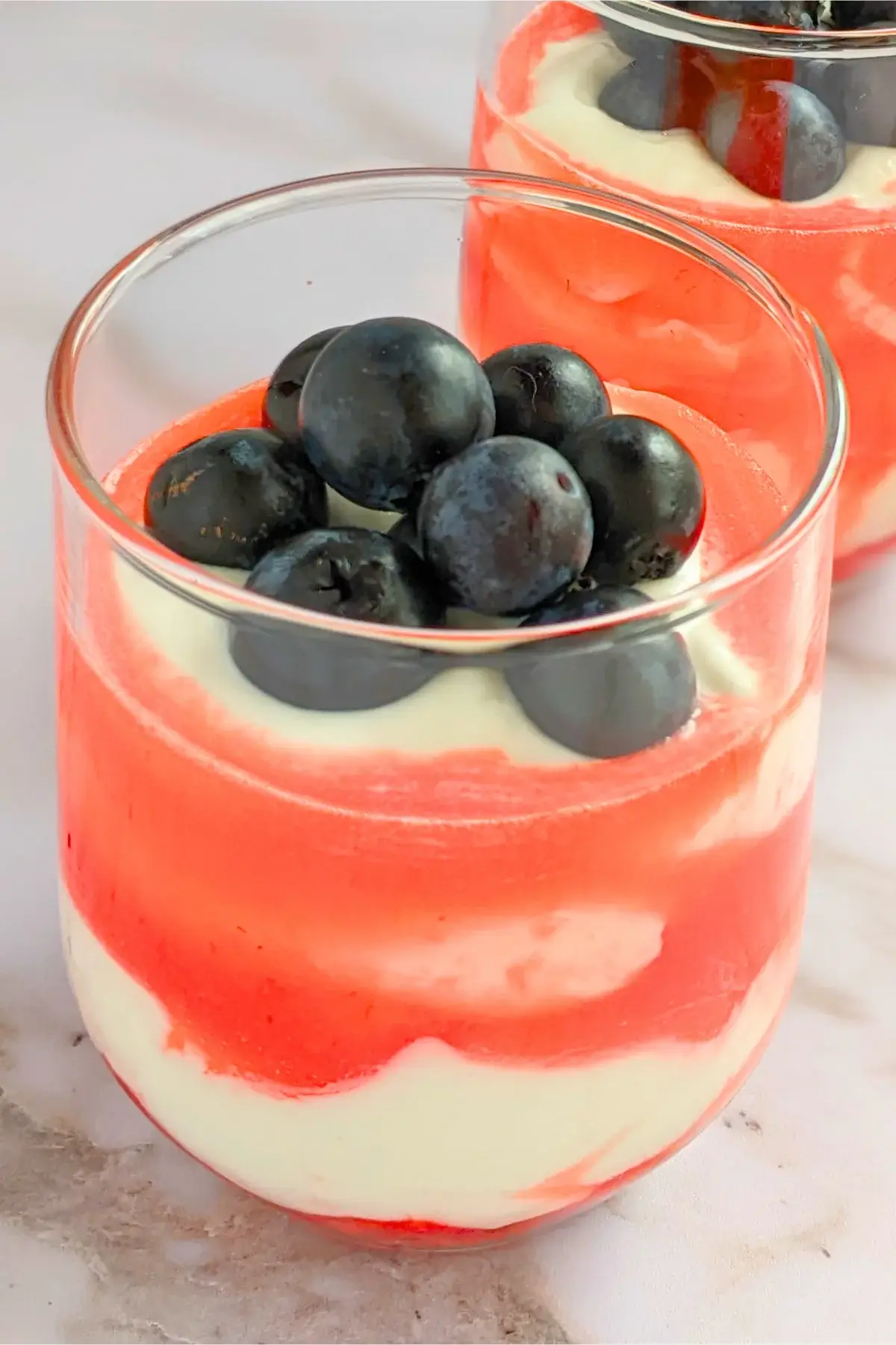 Layered healthy mixed berry fool cups with strawberries, whipped cream, strawberry juice, and blueberries.