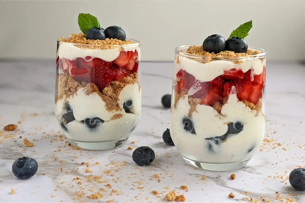 Parfait cups filled with layers of Greek yogurt, oat cookies, strawberries, blueberries, and a drizzle of honey.