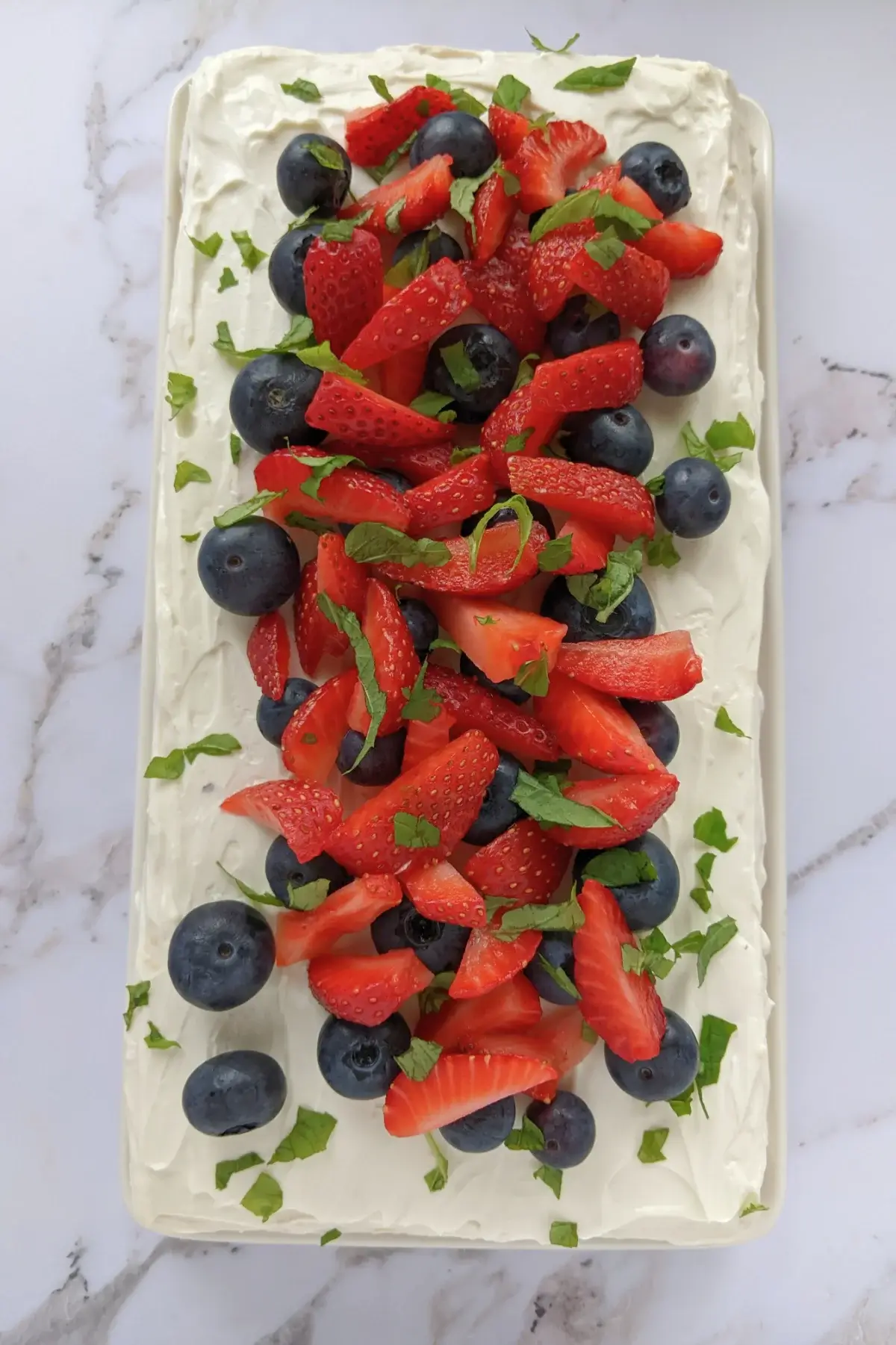 Triple-layer Berry sponge cake with ricotta frosting, topped with fresh strawberries and blueberries.