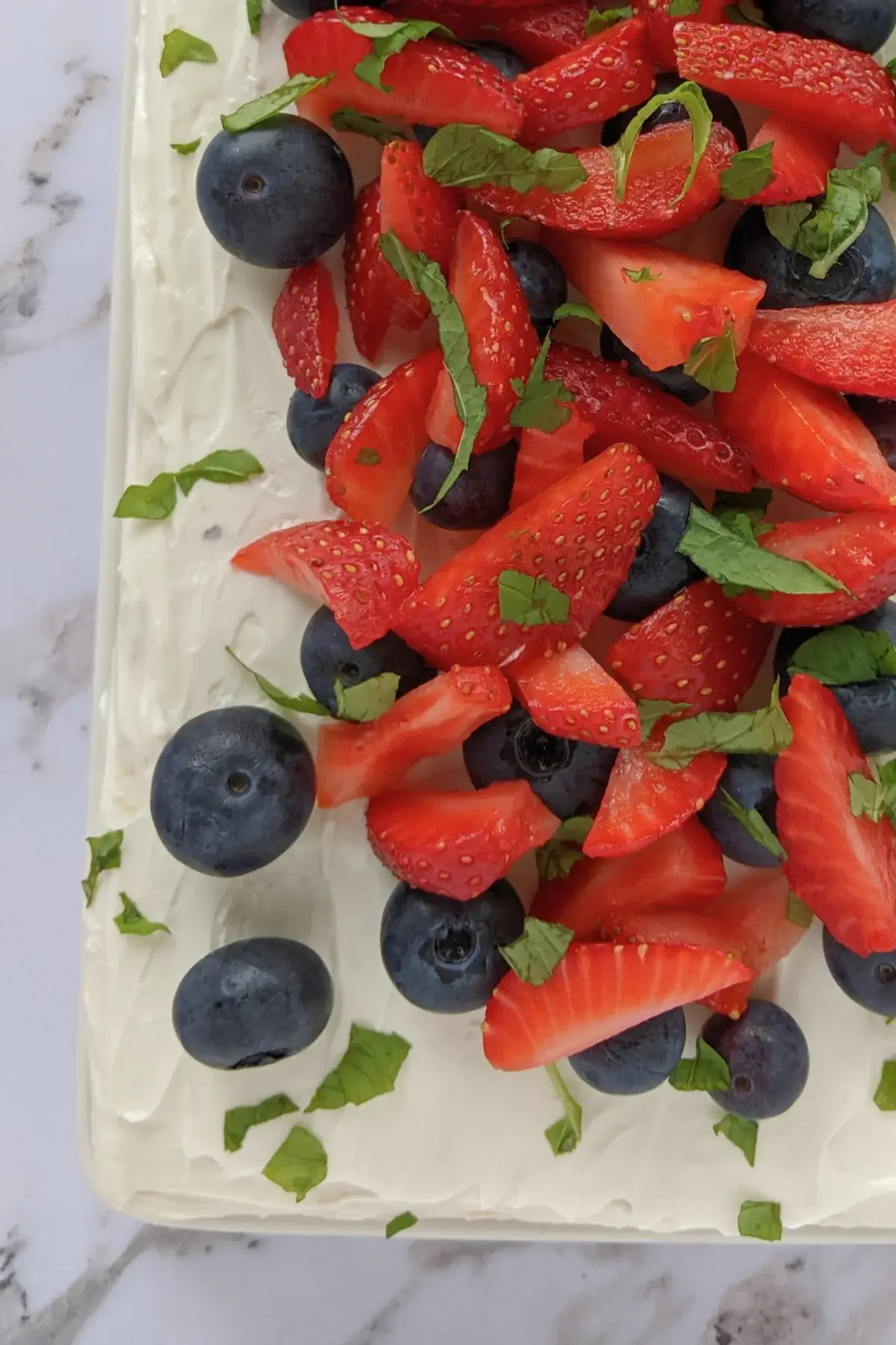 Triple-layer berry sponge cake with ricotta frosting topped with fresh blueberries and strawberries on a white cake stand.
