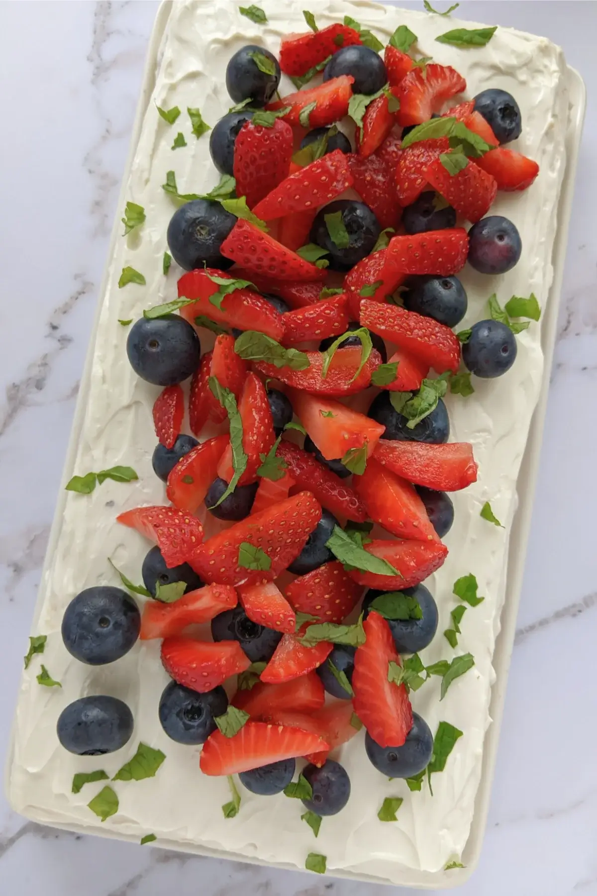 Layered sponge cake with berries and ricotta frosting, topped with fresh strawberries and blueberries.