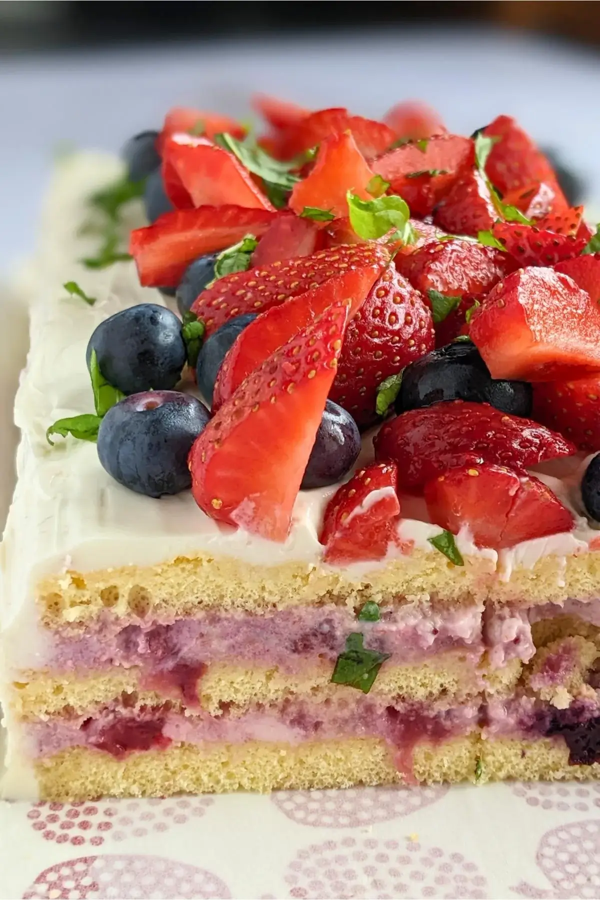 Tall sponge cake with three layers, filled with mascarpone-Greek-yogurt-ricotta cream and berry compote, frosted with mascarpone and topped with fresh mixed berries.
