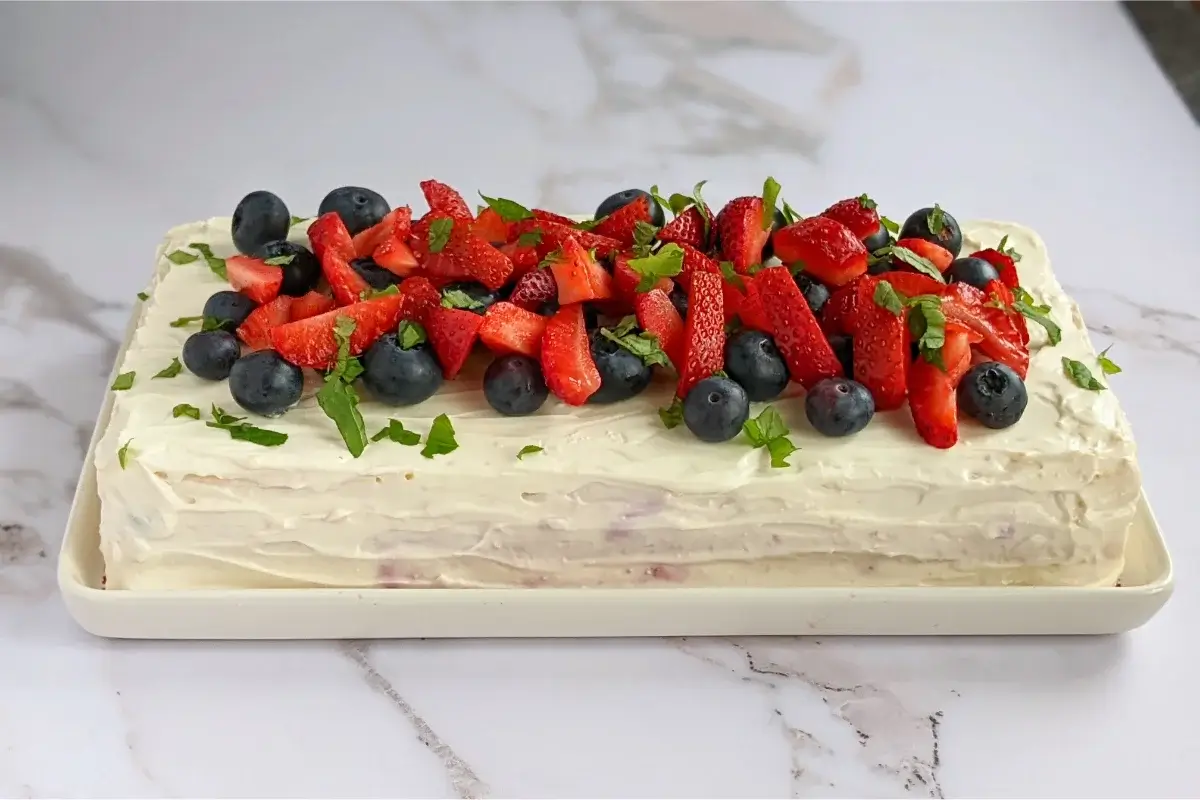 Tall sponge cake with three layers, filled with mascarpone-Greek-yogurt-ricotta cream and berry compote, frosted with mascarpone and topped with fresh mixed berries.