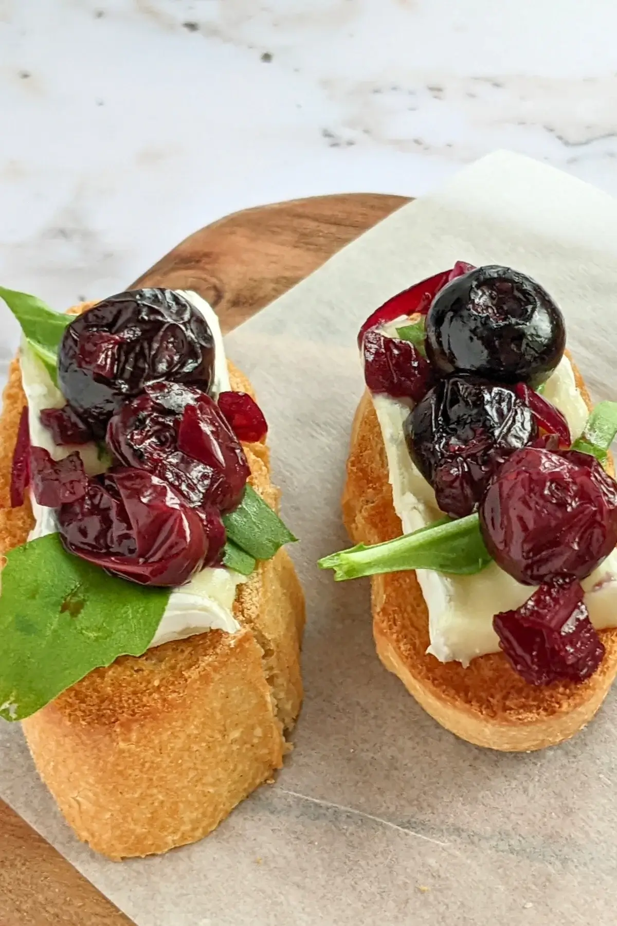 Blueberry crostini topped with brie, caramelized onions, and arugula on toasted bread slices.