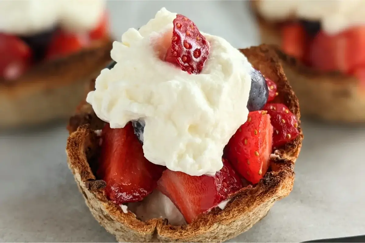 Crispy bread cups filled with fresh berries and topped with a swirl of whipped cream for a light dessert bite.