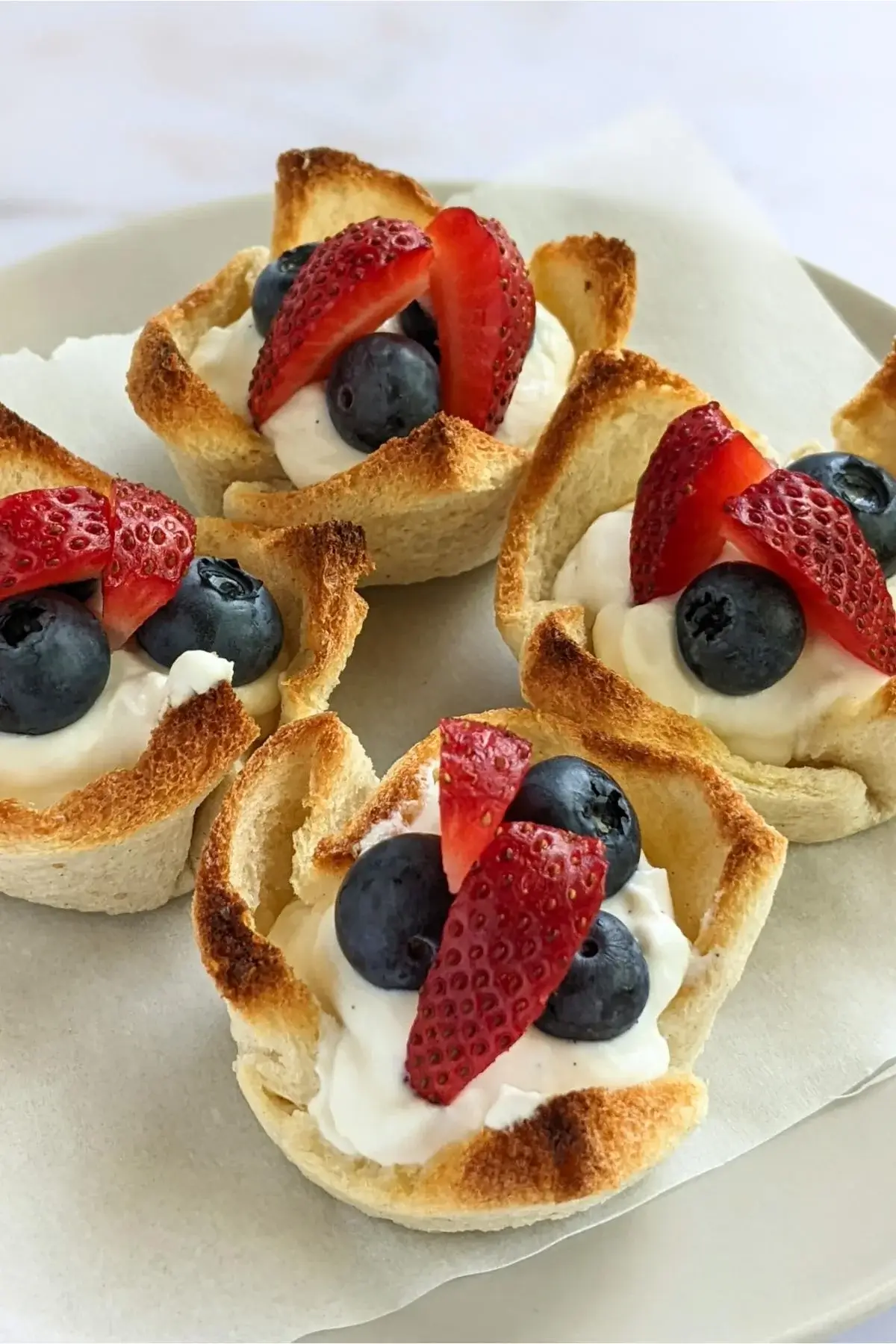 White bread cups filled with sweet whipped ricotta and topped with fresh strawberries and blueberries for a healthy summer treat.