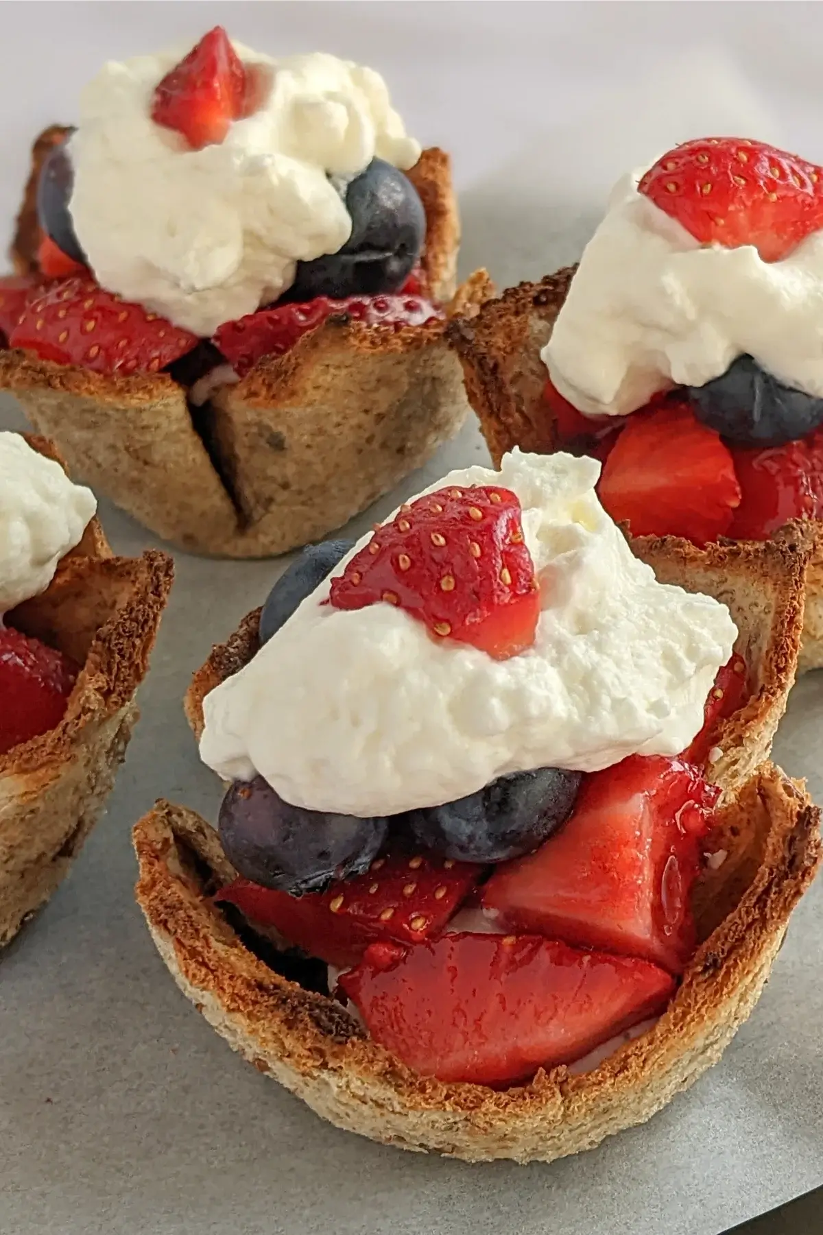 Wholemeal bread cups filled with berry compote and whipped cream on a rustic wooden board.