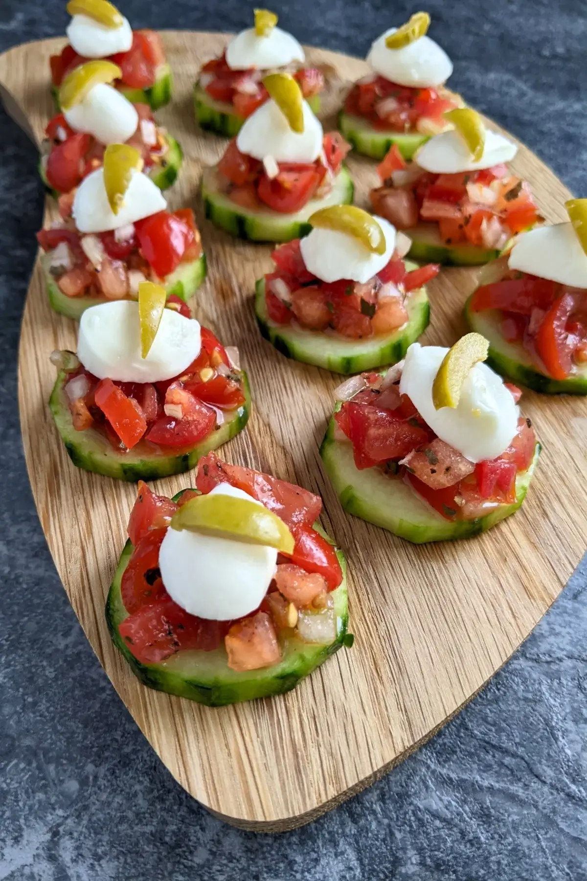 Fresh bruschetta cucumber bites topped with mozzarella balls and sliced olives, neatly arranged on a serving tray.