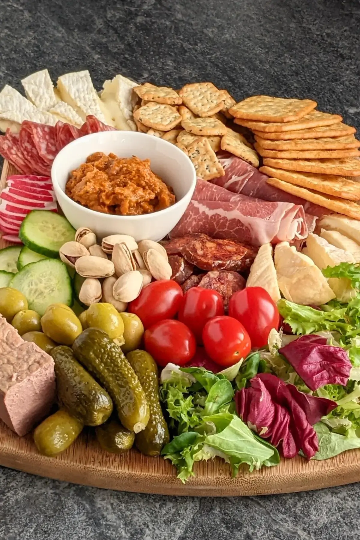 A balanced charcuterie board with some meats, soft cheeses, and plenty of fresh vegetables and pickles.