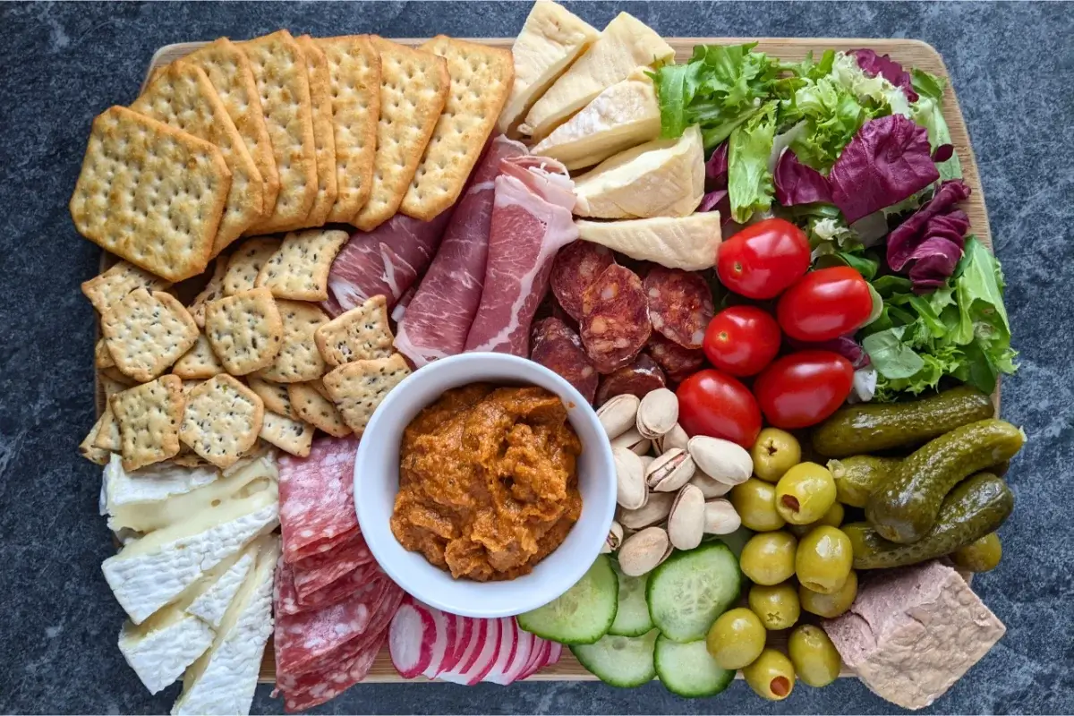 A balanced charcuterie board with some meats, soft cheeses, and plenty of fresh vegetables and pickles.