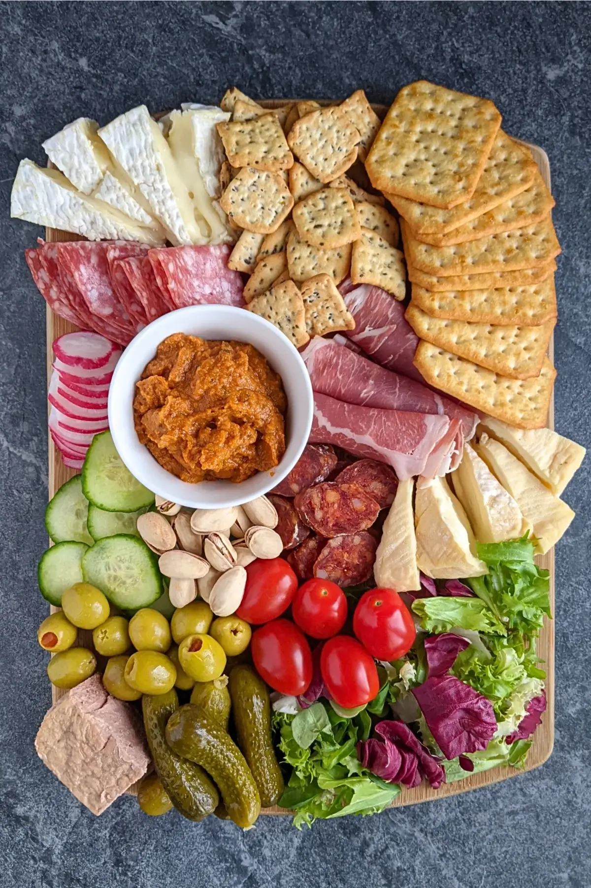 A healthier charcuterie board featuring fresh vegetables, soft cheeses, sliced meats, and pickled bites on a rustic board.