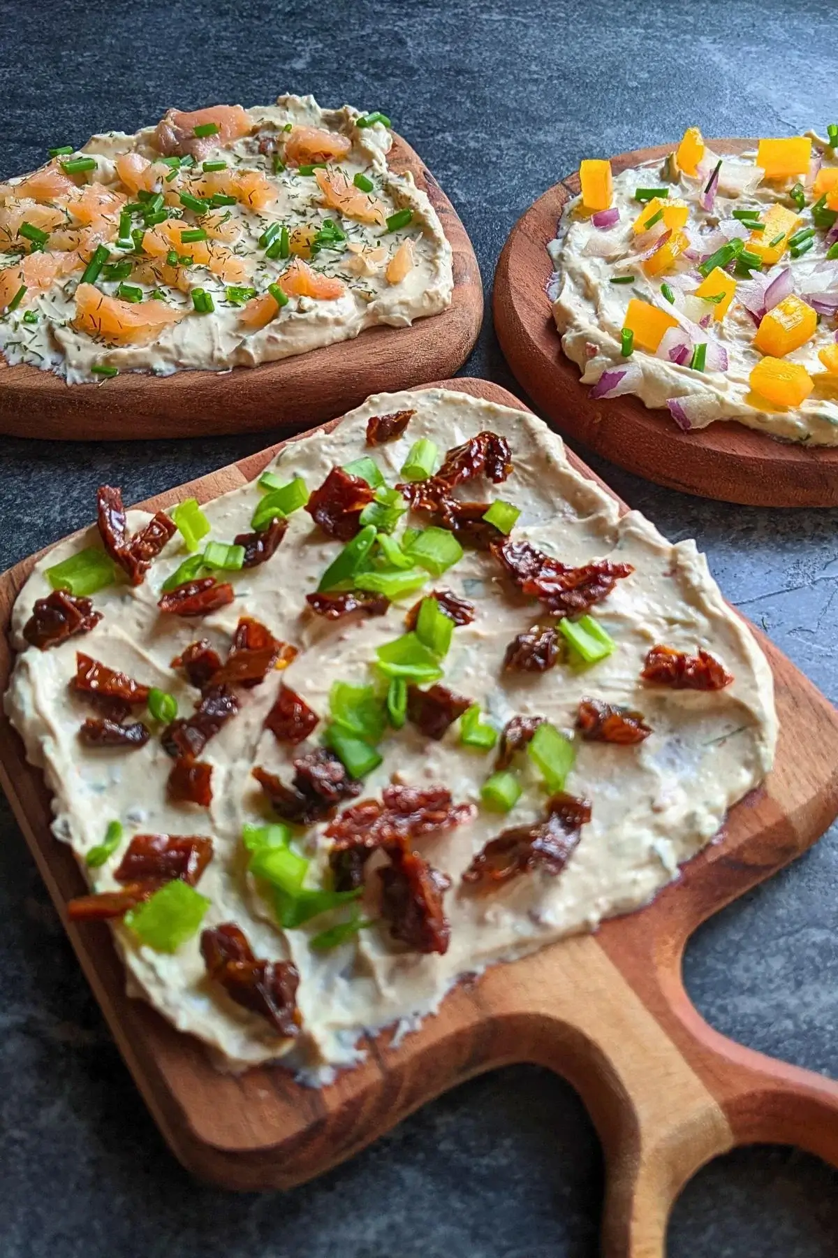 Feta cheese spread boards with a mix of savory toppings like red onion and yellow capsicum, sundried tomatoes and green onion, and smoked salmon and chives.