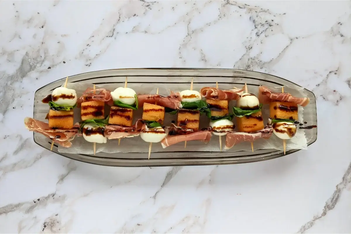 Skewers with sweet melon, salty prosciutto, and creamy mozzarella, finished with basil and balsamic drizzle.