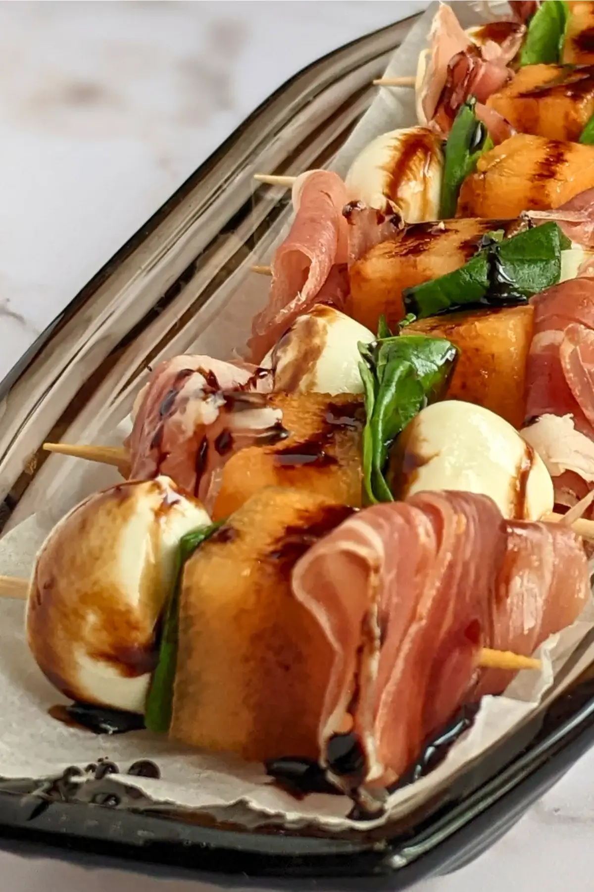 Melon, prosciutto & mozzarella skewers garnished with fresh basil and a balsamic glaze.