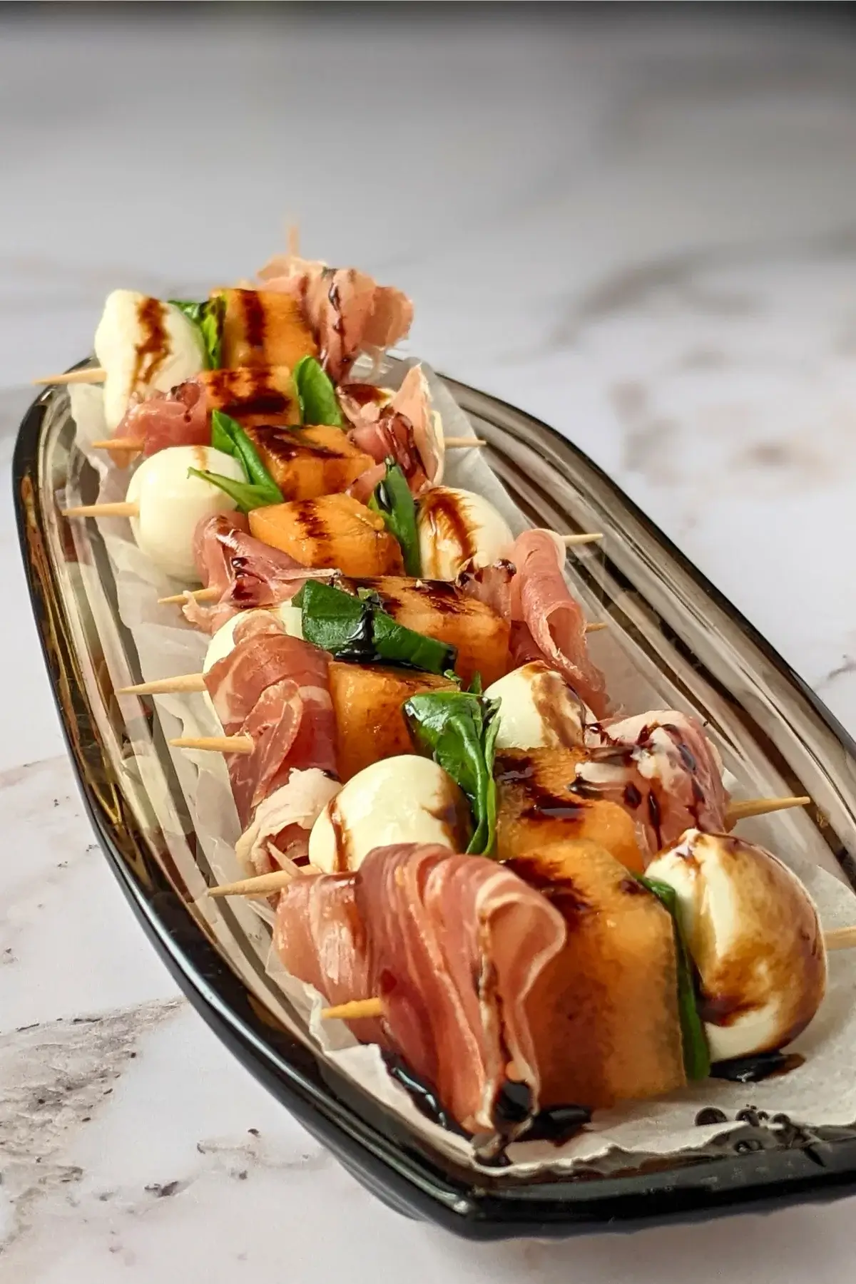 Skewers of melon, mozzarella, and prosciutto with fresh basil and balsamic drizzle.