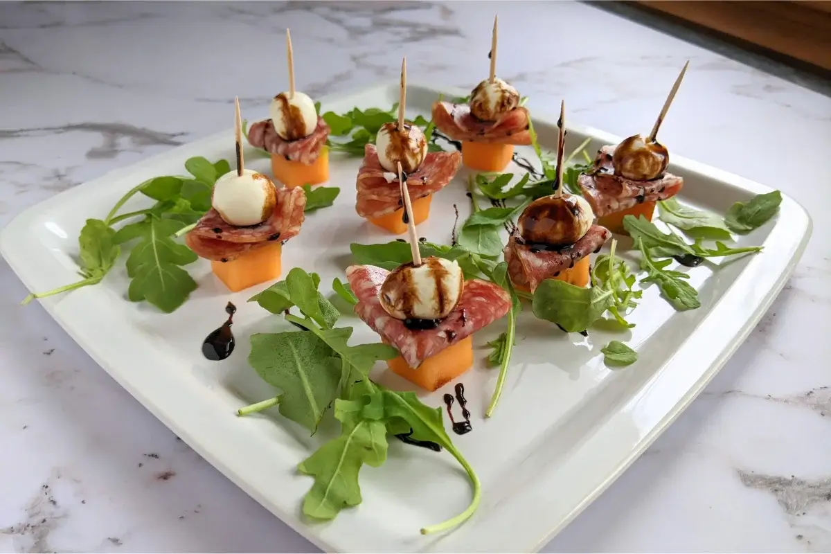 Skewers combining melon, salami, and mozzarella, drizzled with balsamic glaze for a sweet and savory flavor.