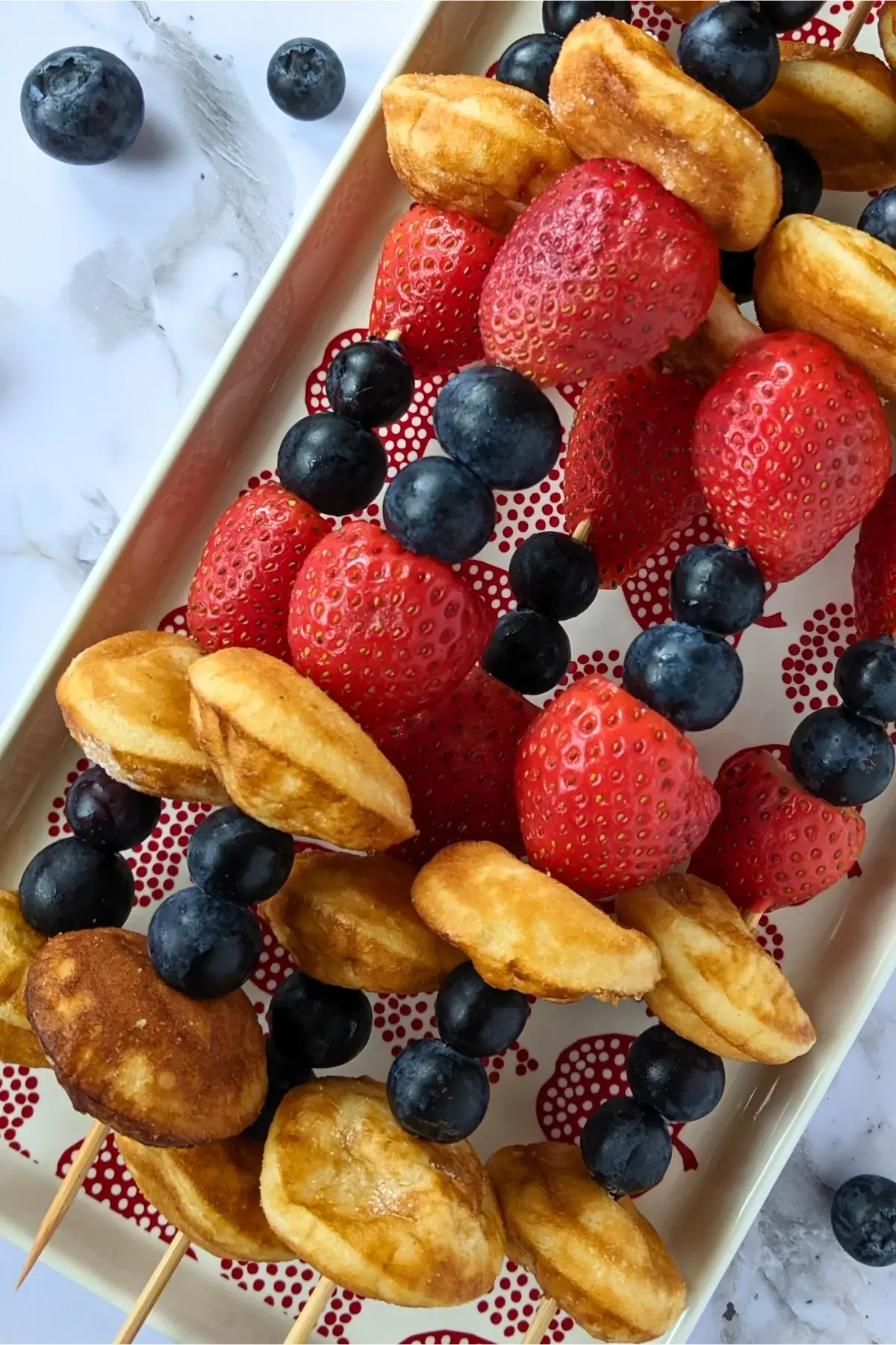 Mini pancake and fresh berry skewers stacked with strawberries and blueberries on wooden picks.