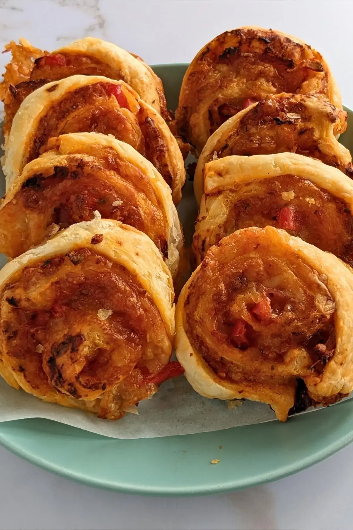Golden puff pastry pizza pinwheels filled with tomato sauce, cheese, and herbs for a savory party snack.