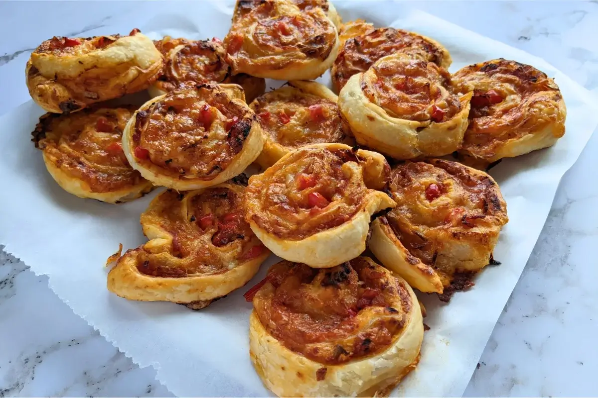 Golden puff pastry pizza pinwheels filled with tomato sauce, cheese, and herbs for a savory party snack.