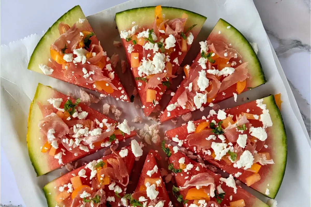 Watermelon slice topped like a pizza with melon slices, prosciutto, and feta.
