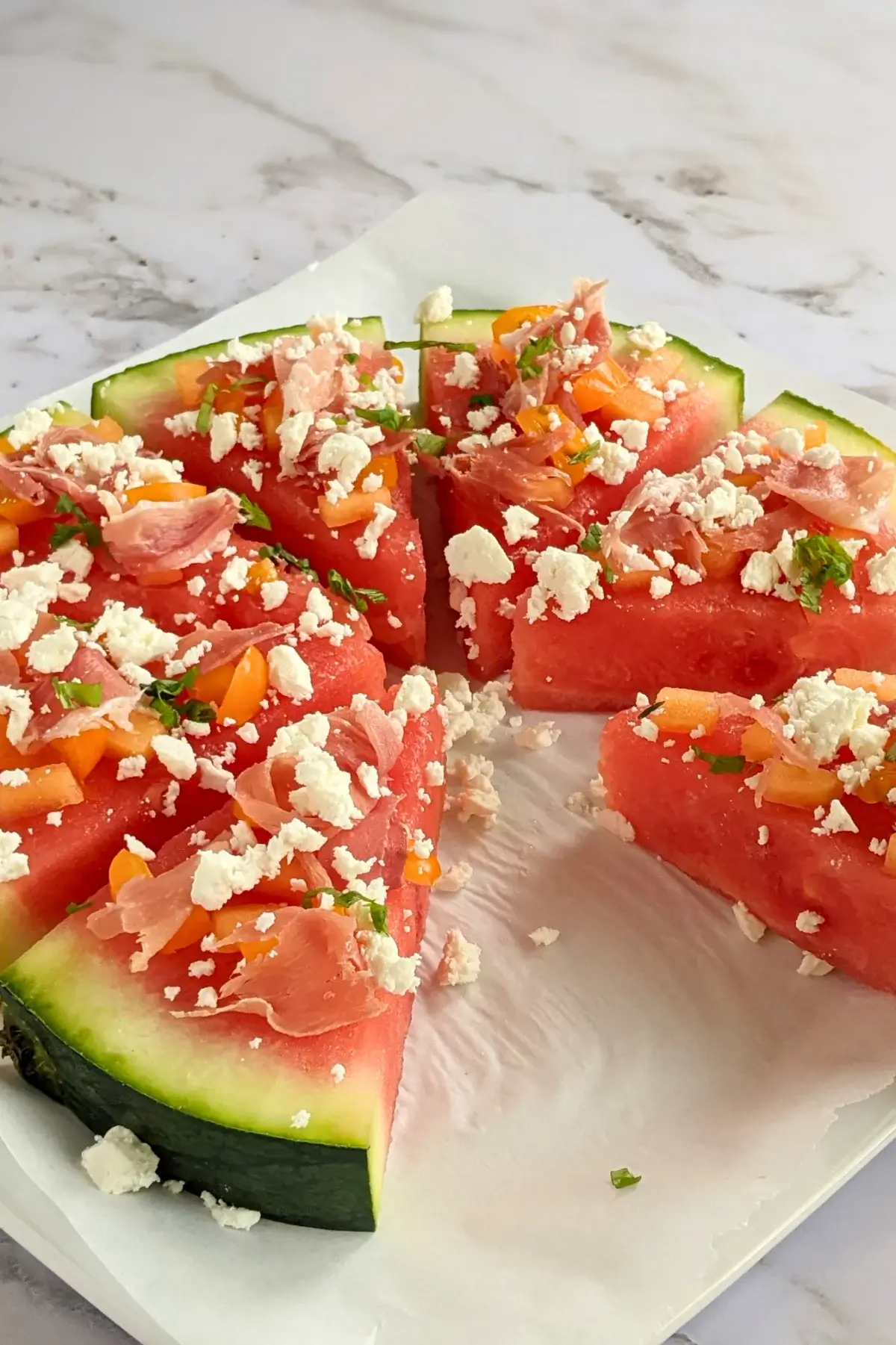 Watermelon slices topped with prosciutto, feta cheese, and basil served like pizza.