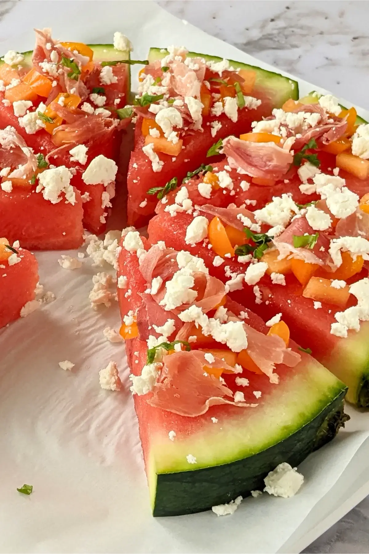 Savory watermelon pizza topped with prosciutto, feta, and fresh basil.