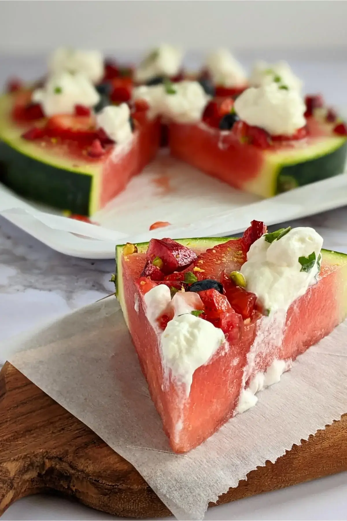 Watermelon slices topped like a pizza with whipped cream, strawberries, blueberries, cherries, and mint.