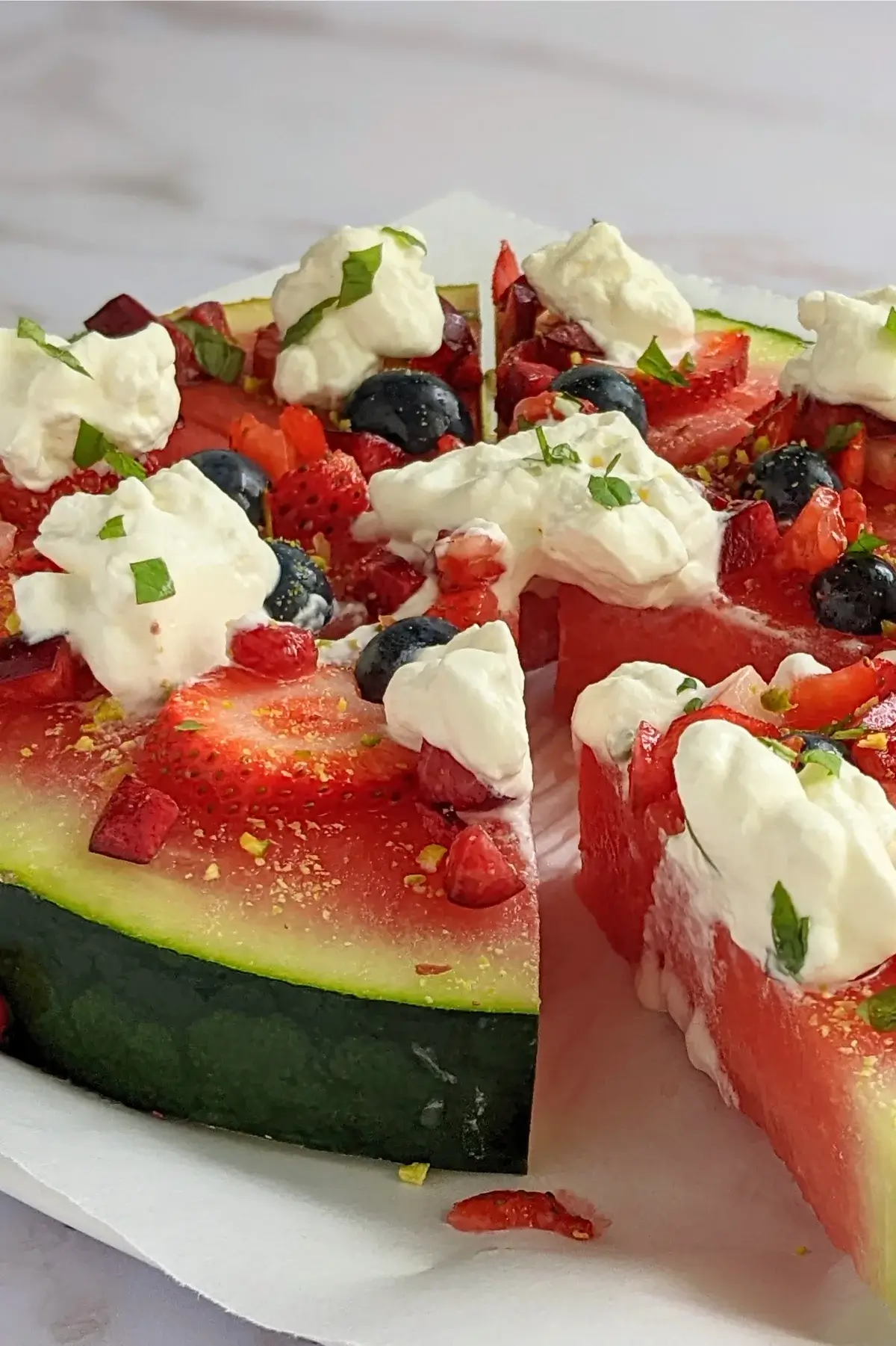 Watermelon pizza with strawberries, blueberries, cherries, whipped cream, and pistachios.