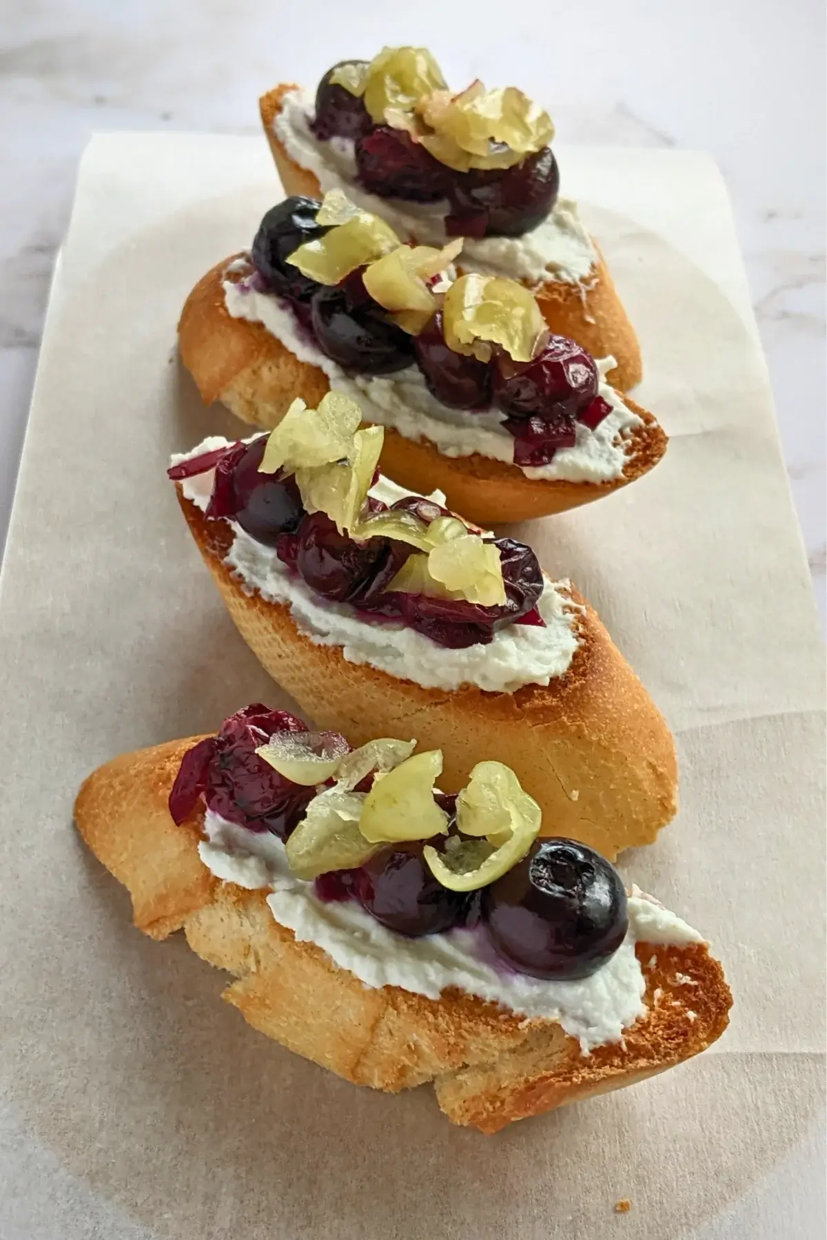 Blueberry bruschetta appetizer - toasted baguette bread topped with ricotta cheese, cooked blueberries, and sliced jalapeños.