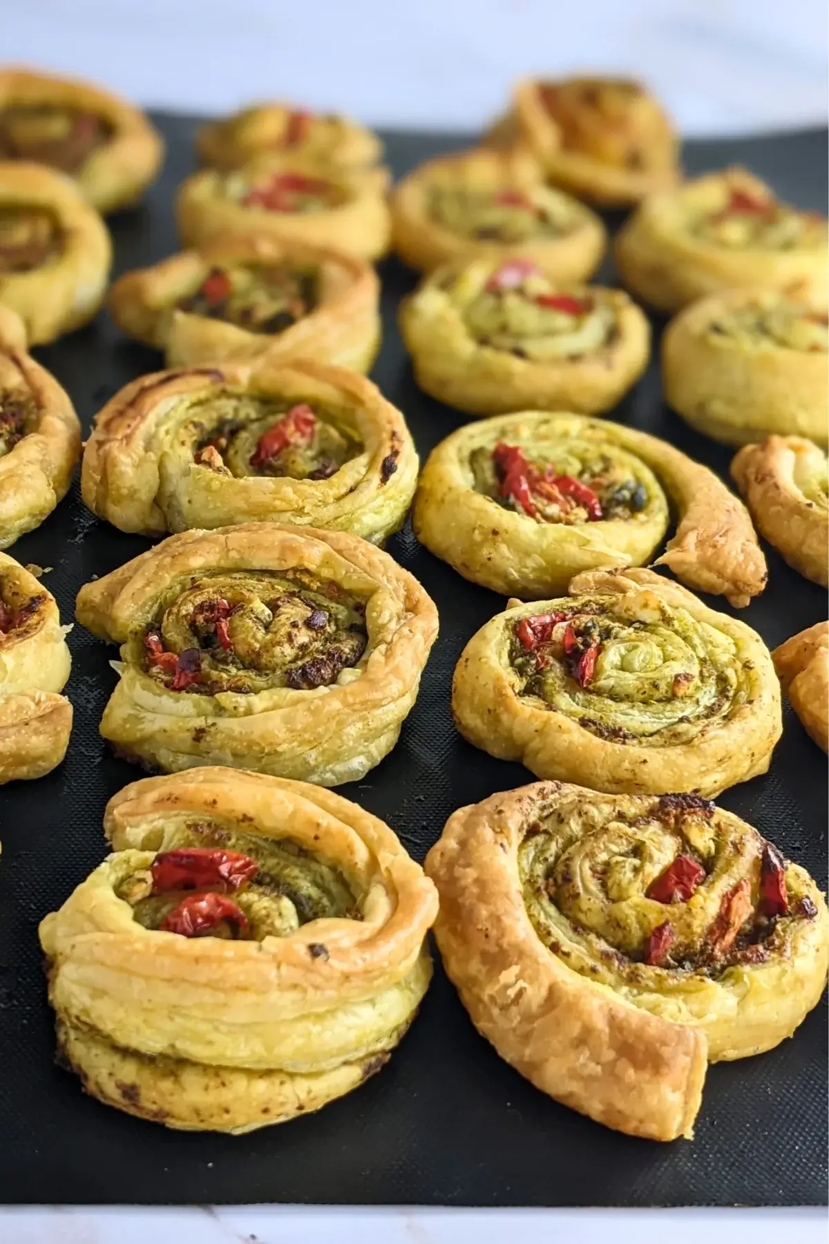 Savory pesto pinwheels filled with basil pesto, sun-dried tomatoes, and crumbled feta.
