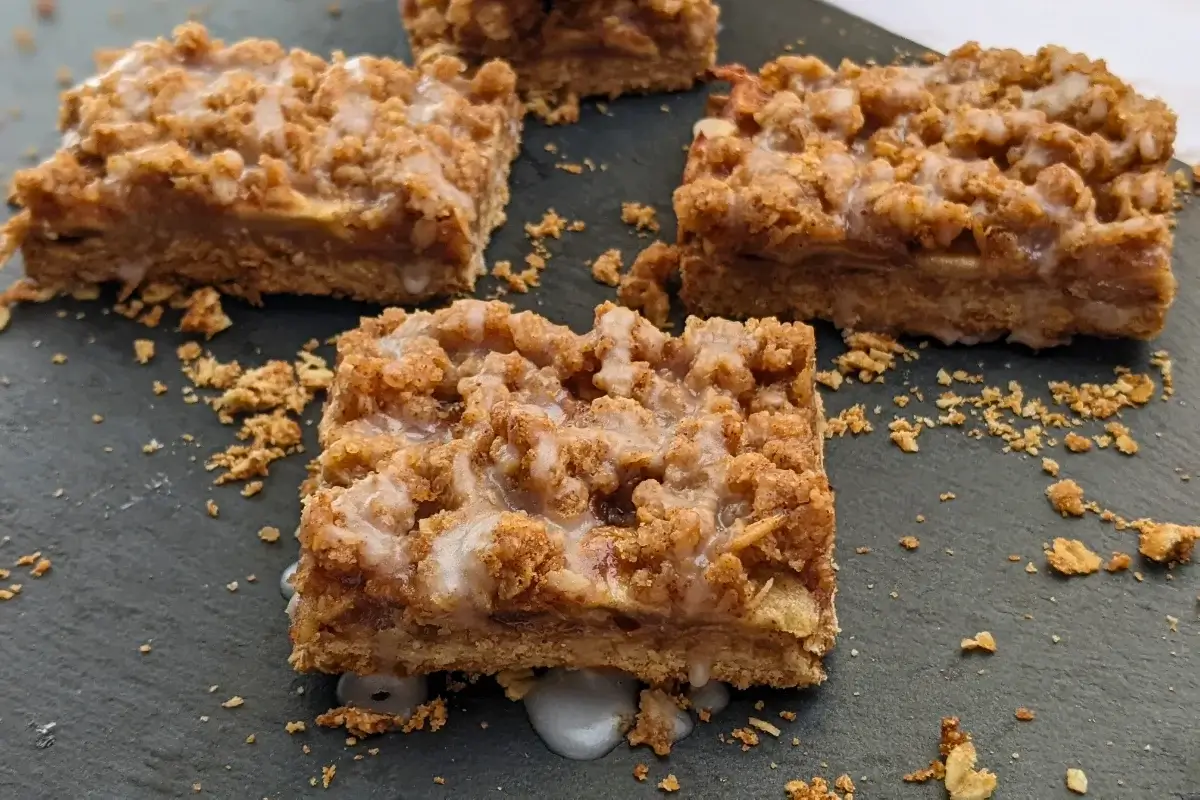 Apple crisp bars made with a flour and oat base, cinnamon apple filling, and streusel topping, drizzled with an icing sugar and milk frosting.
