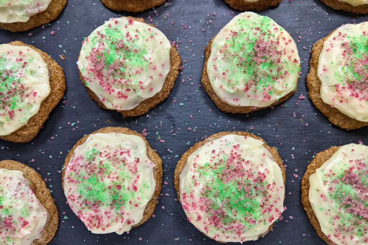 Christmas pumpkin sugar cookies made with healthier wholemeal flour and coconut sugar, frosted with a classic butter and cream cheese icing, and decorated with red and green sugar sprinkles.