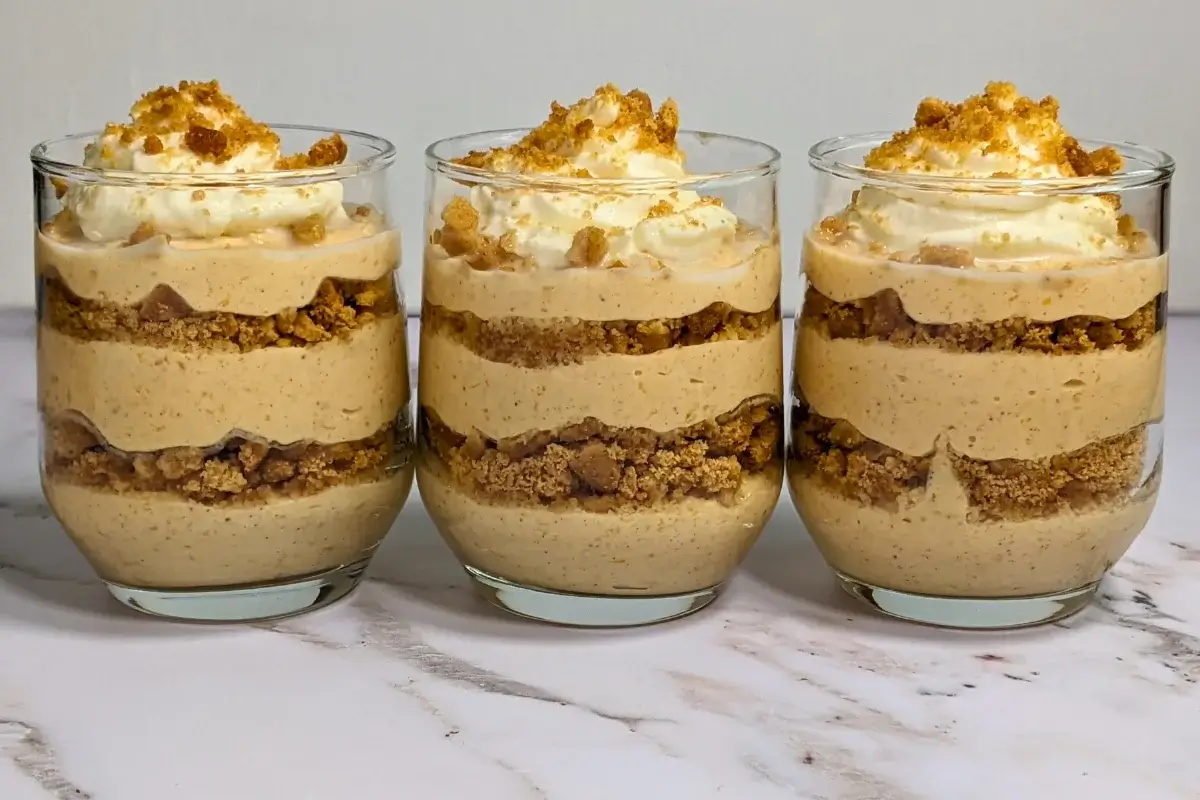 Pumpkin yogurt parfait cups layered with pumpkin yogurt, gingersnap biscuits, and topped with whipped cream.
