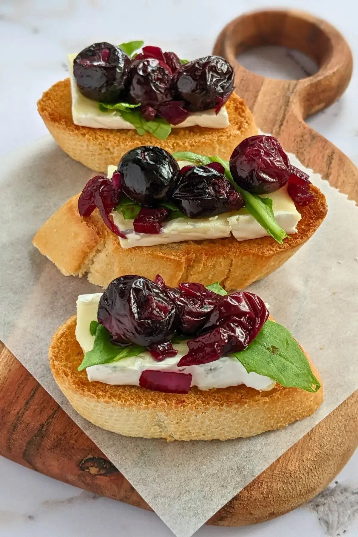 Blueberry crostini topped with brie, caramelized onions, and arugula on toasted bread slices.