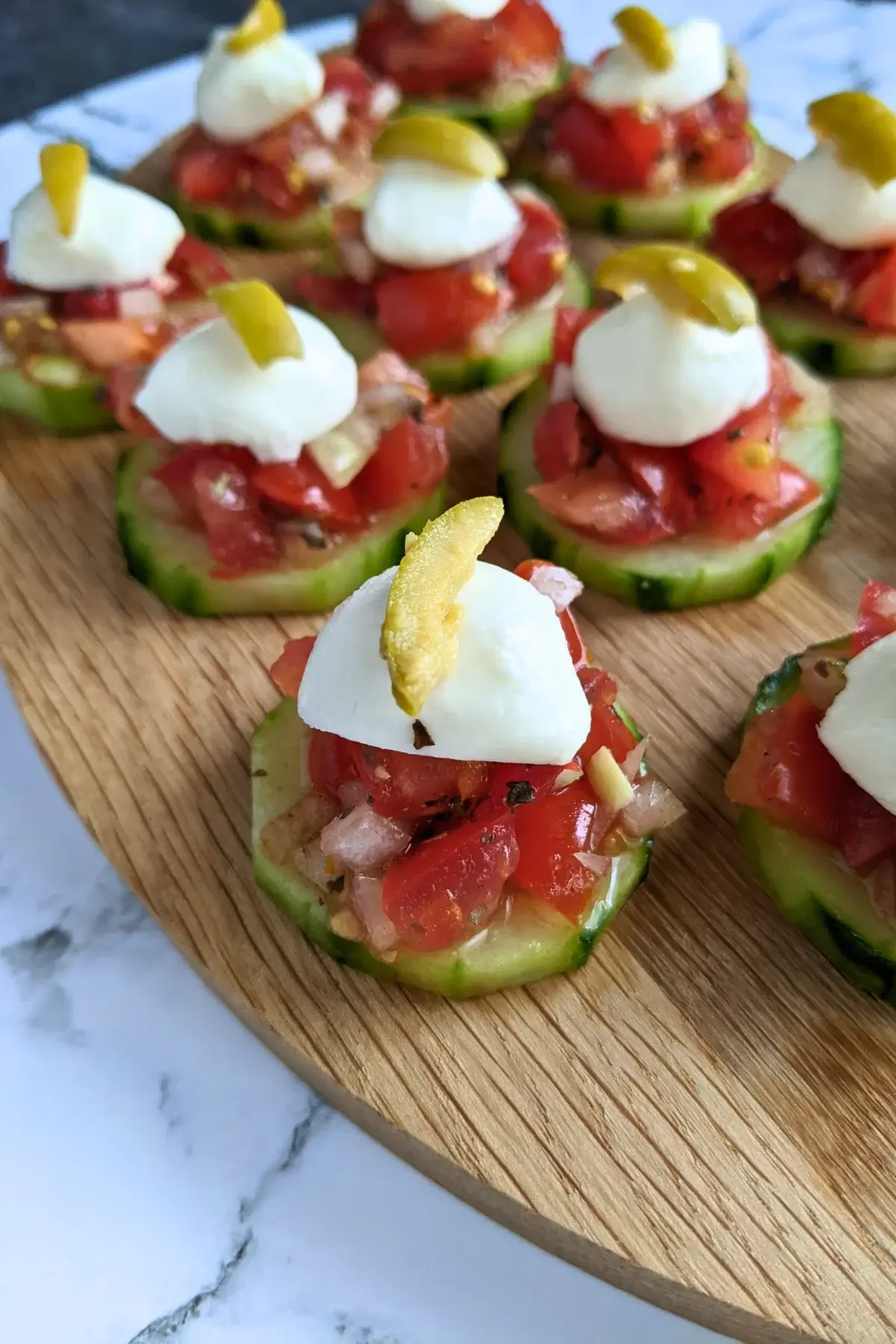 Fresh bruschetta cucumber bites topped with mozzarella balls and sliced olives for decoration.