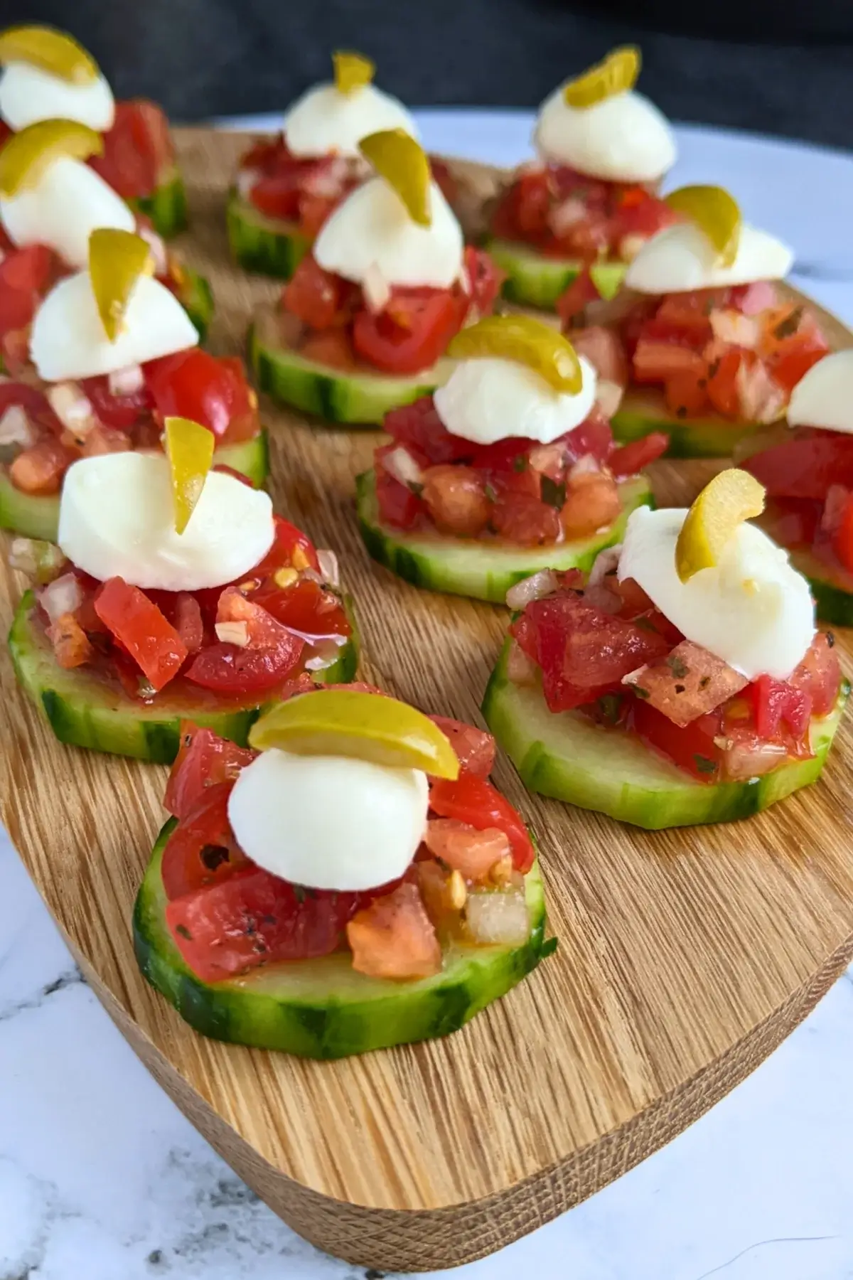 Fresh bruschetta cucumber bites topped with mozzarella balls and sliced olives for decoration.