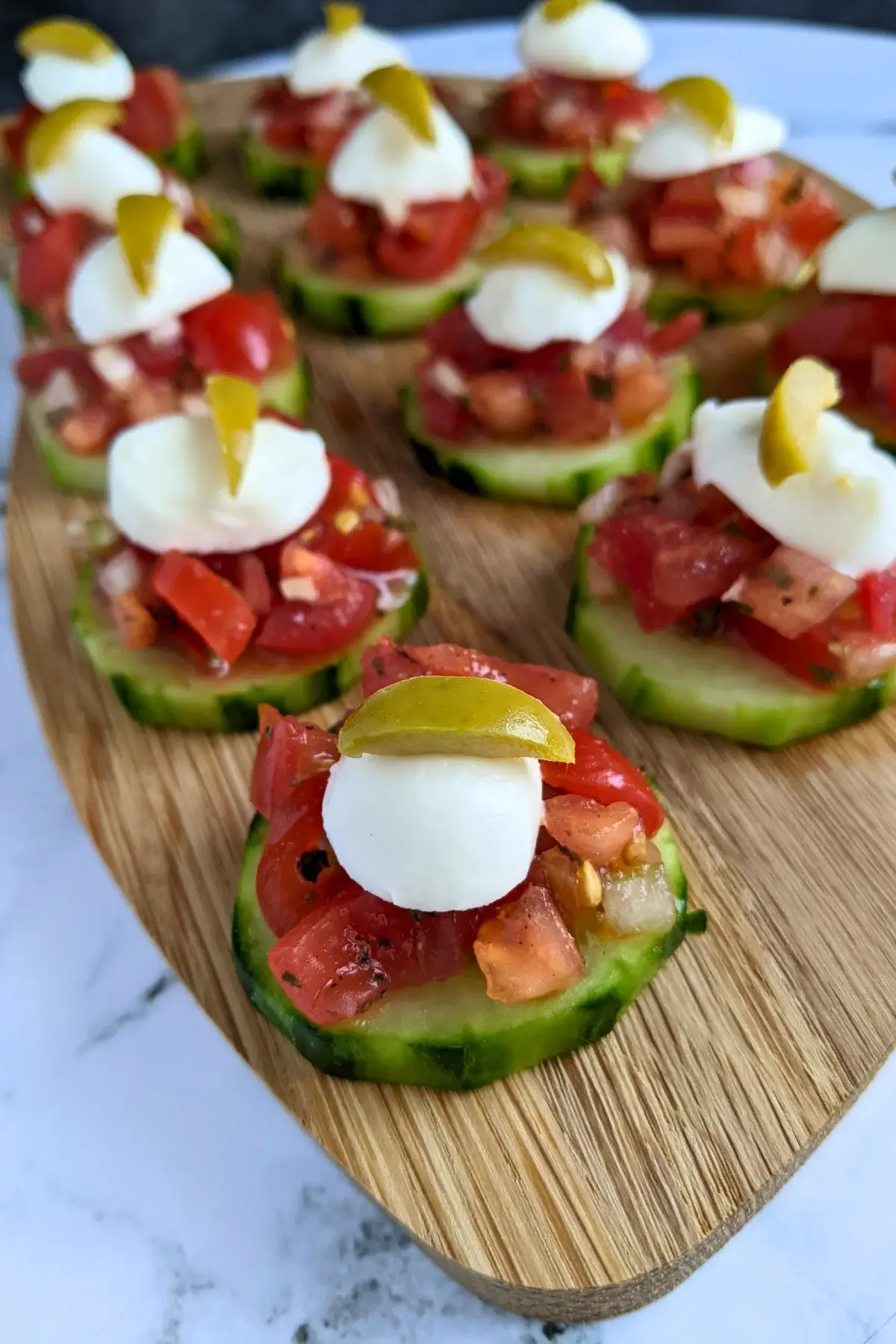 Fresh bruschetta cucumber bites topped with mozzarella balls and sliced olives, neatly arranged on a serving tray.