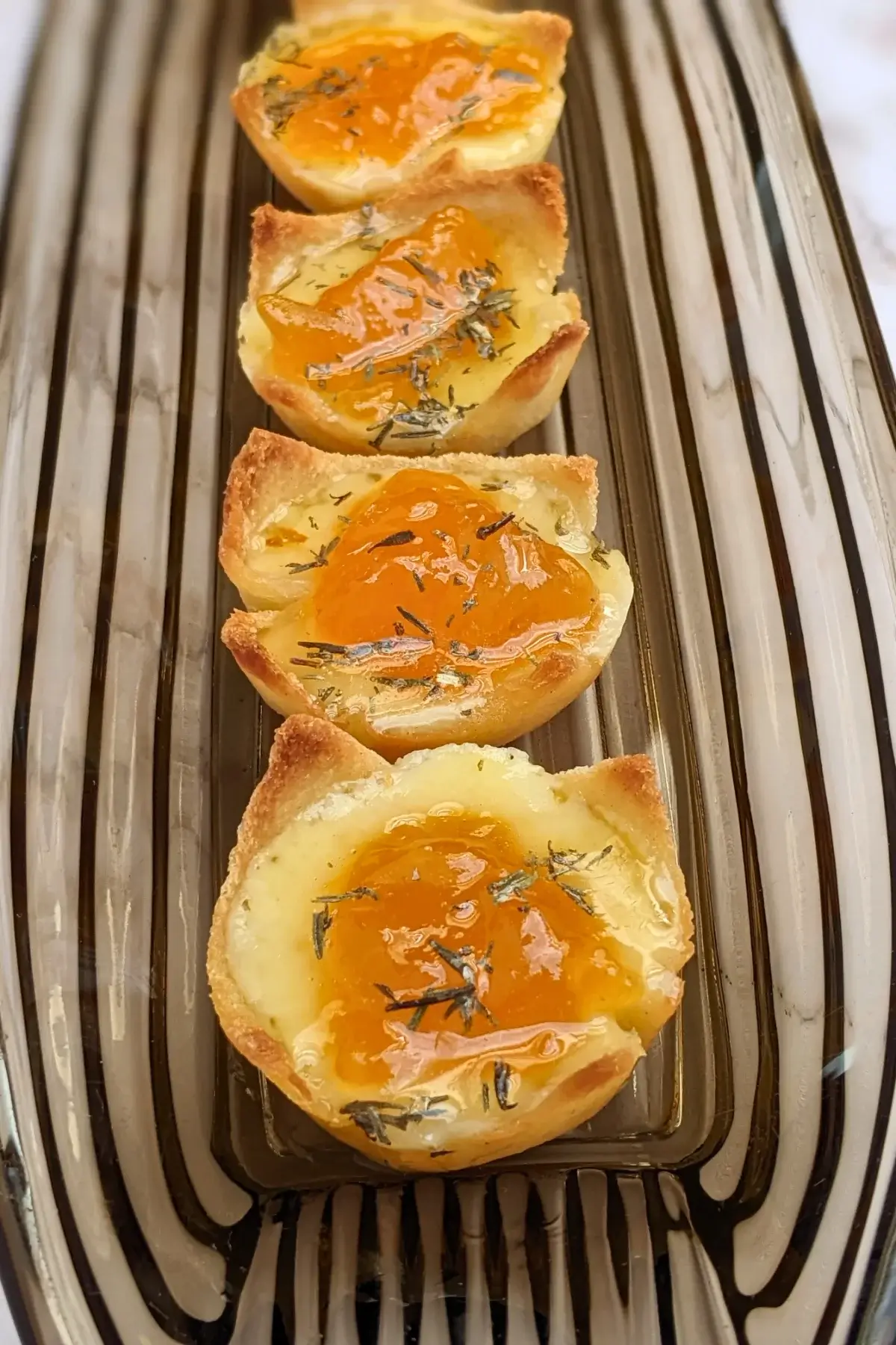 Cheddar cheese and apricot jam appetizer bites - mini bread toast cups filled with cheddar cheese, topped with apricot jam and a honey-dryed thyme drizzle.