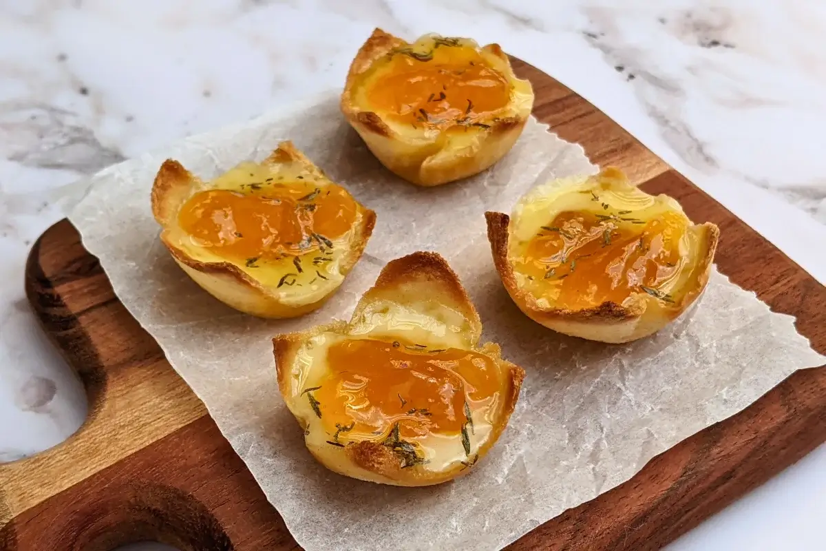 Cheddar cheese and apricot jam appetizer bites - mini bread toast cups filled with cheddar cheese, topped with apricot jam and a honey-dryed thyme drizzle.