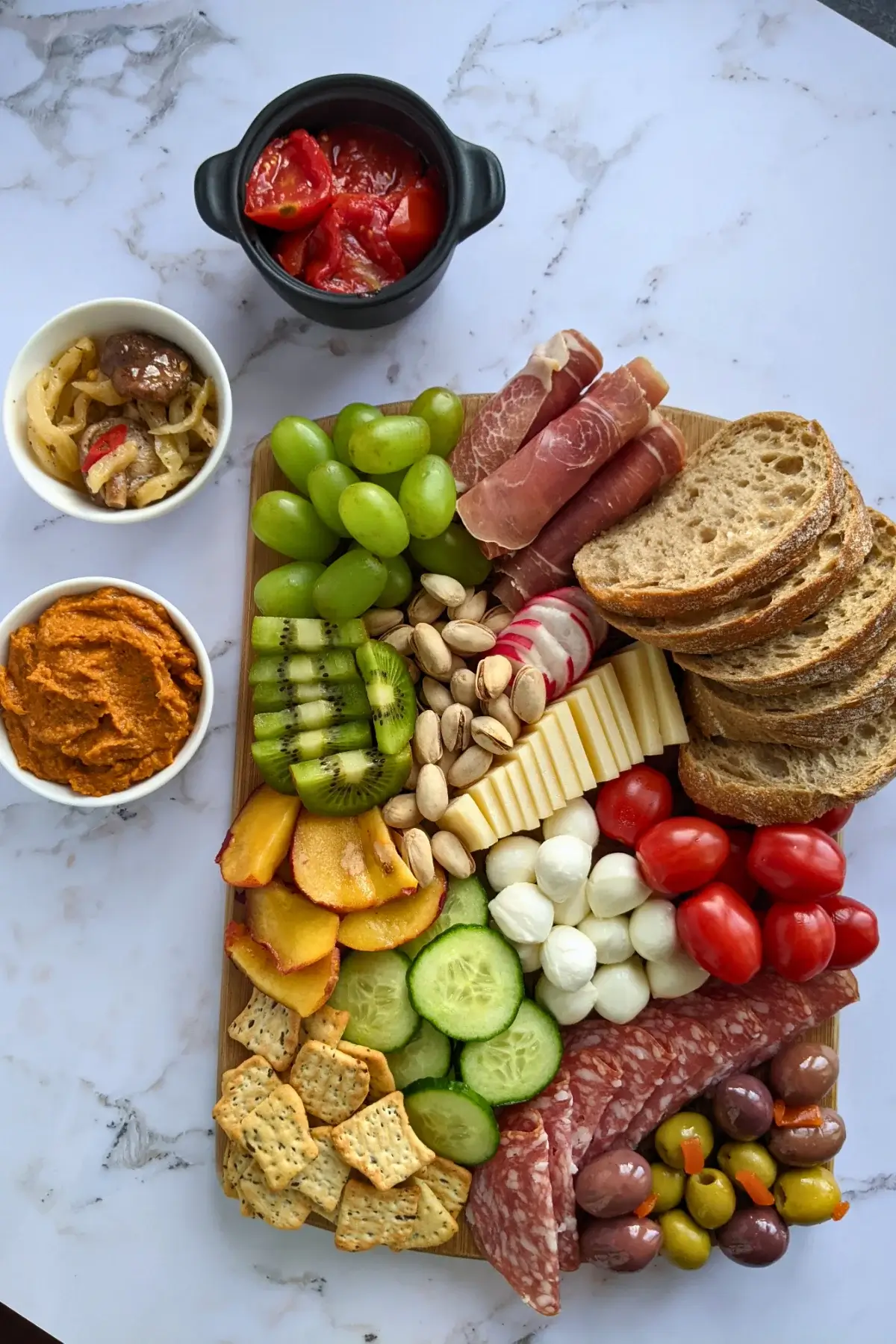 A vibrant antipasto board featuring salami, prosciutto, marinated tomatoes, olives, cheese, and fresh fruit.