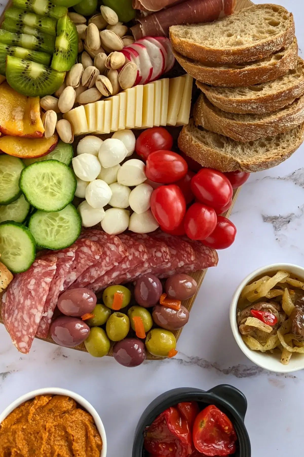 A vibrant colorful antipasto board with cured meats, marinated veggies, cheeses, olives, fruit, and ciabatta arranged on a wooden platter.