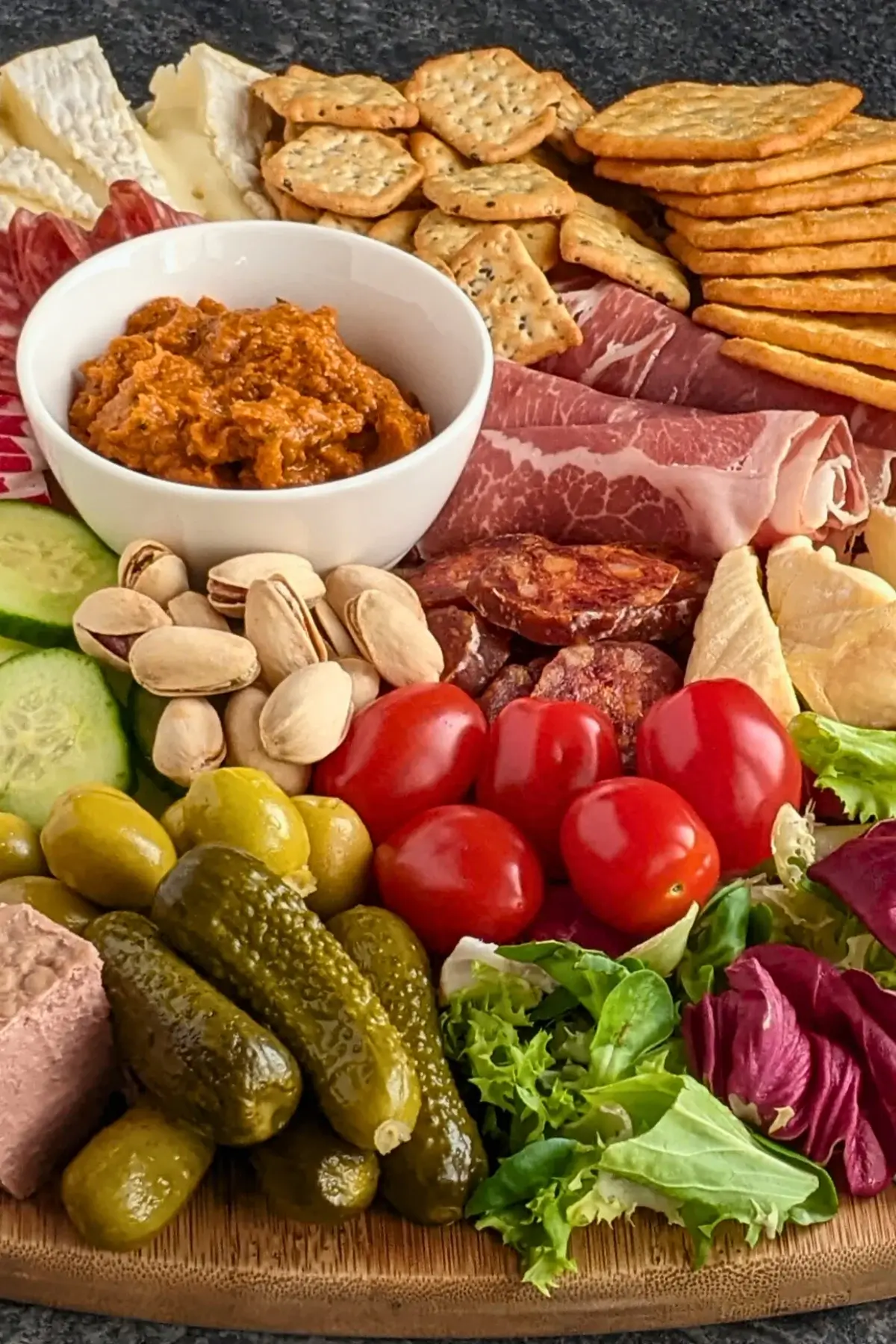 A healthier charcuterie board featuring fresh vegetables, soft cheeses, sliced meats, and pickled bites on a rustic board.